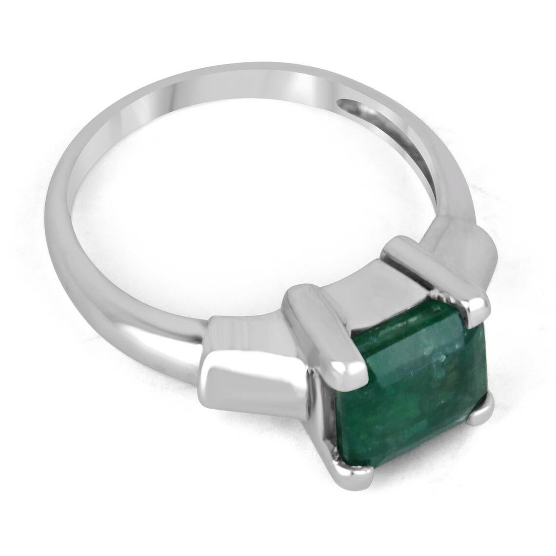Featured is a bold solitaire emerald engagement/right-hand ring. This luxurious piece showcases a remarkable 2.15-carat, natural Asscher cut Zambian emerald, displaying lush bluish-green color, veyr good luster, and many more mesmerizing
