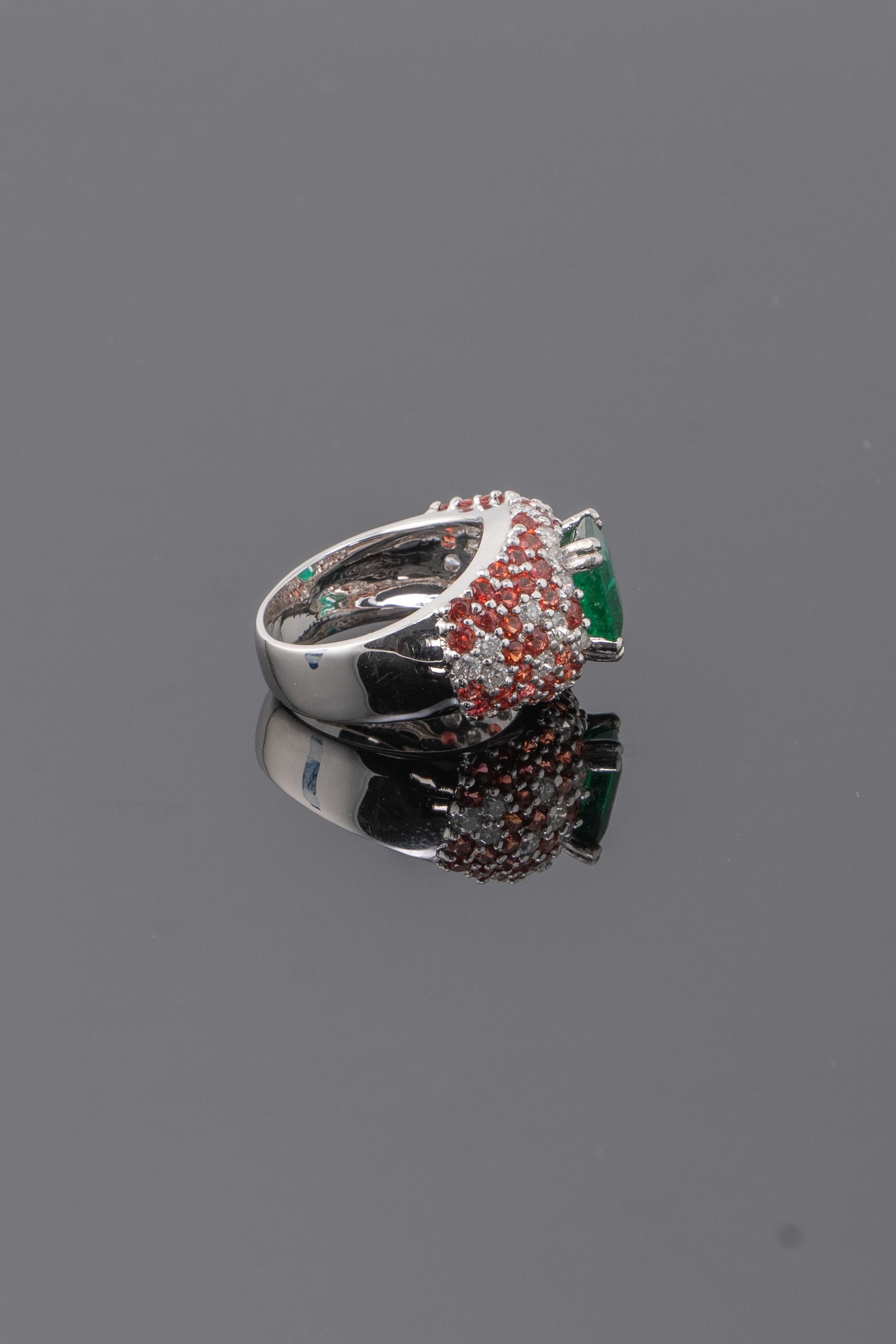 An splendid cocktail ring, with a 2.16 carat transparent natural Zambian Emerald center stone surrounded with sparkling diamonds and magnificent round eye clean orange sapphires . The emerald is transparent with good luster and color, with few
