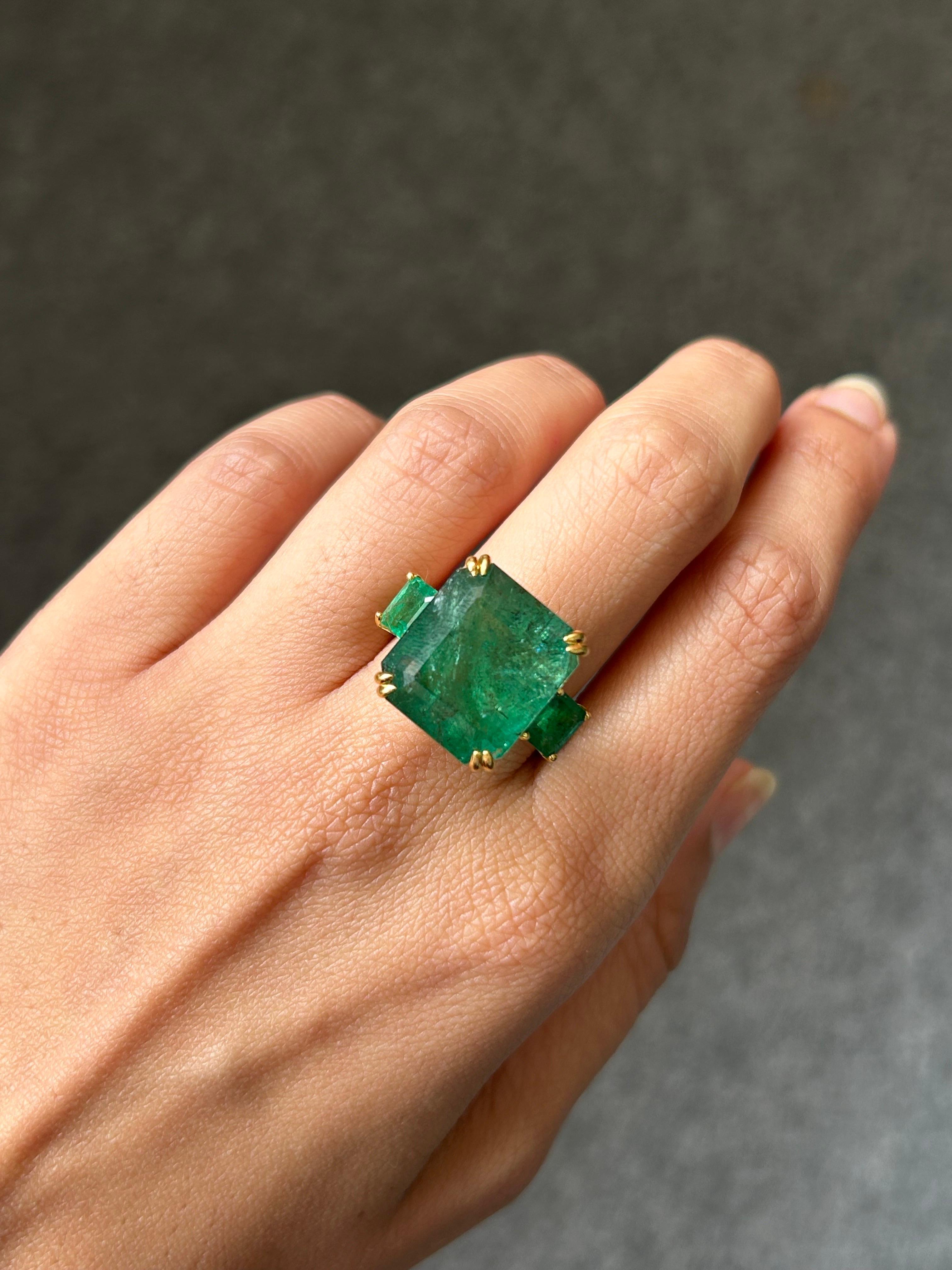 Make a statement with this three stone cocktail ring, with 19.69 carat center stone Zambian Emerald with 2.01 carat side-stone Emeralds. All set in 18K Yellow Gold. The unique feature of this ring is the beautiful green enamel on the band. Currently
