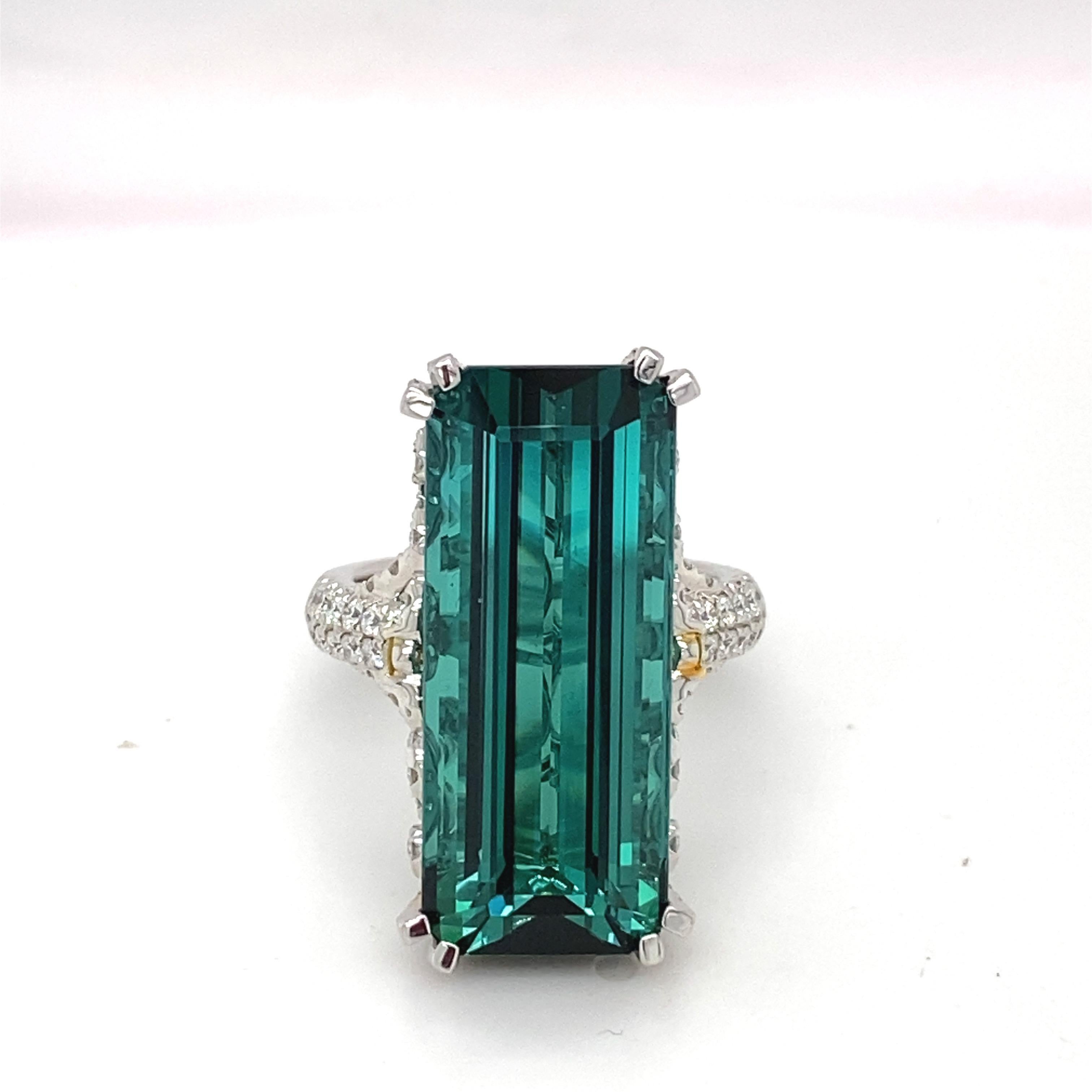 This magnificent 21.86 carat baguette cut Indicolite Tourmaline Diamond ring is mounted in white gold. This exceedingly feminine ring dazzles with the richness and delicacy of it detail work accented with white and yellow diamond. This ring is a