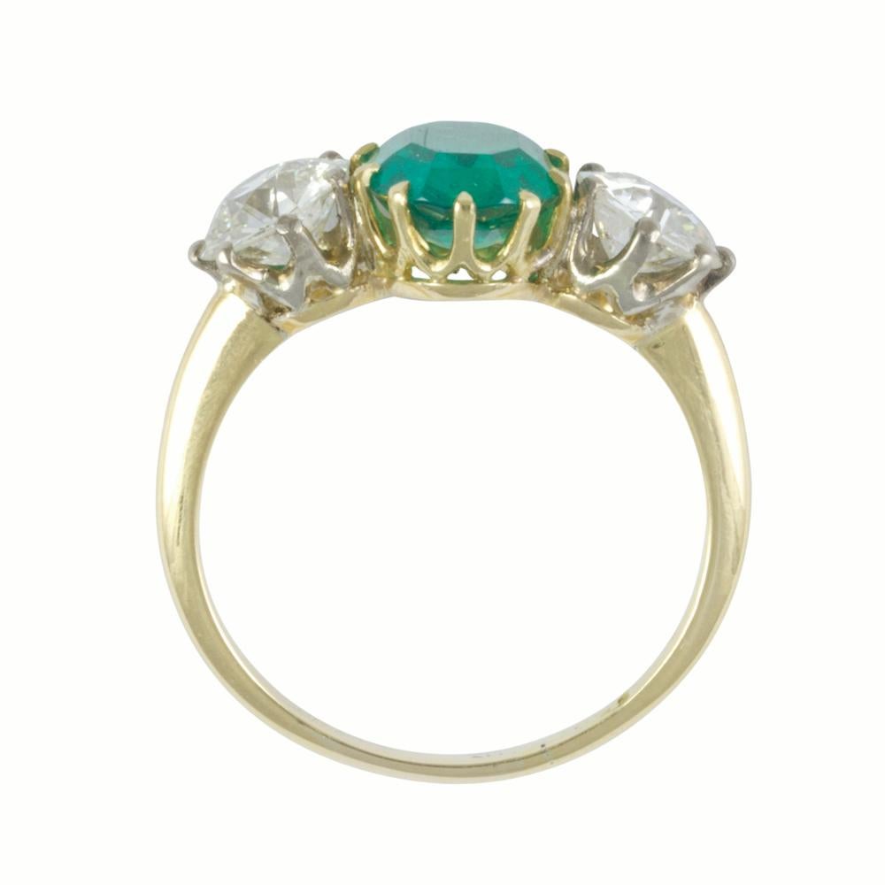 An emerald and diamond three stone ring, the oval faceted emerald weighing 2.19 carats, set to the centre of two round old brilliant-cut diamonds weighing 1.91 carats in total, all claw-set in gold to a D-section shank.