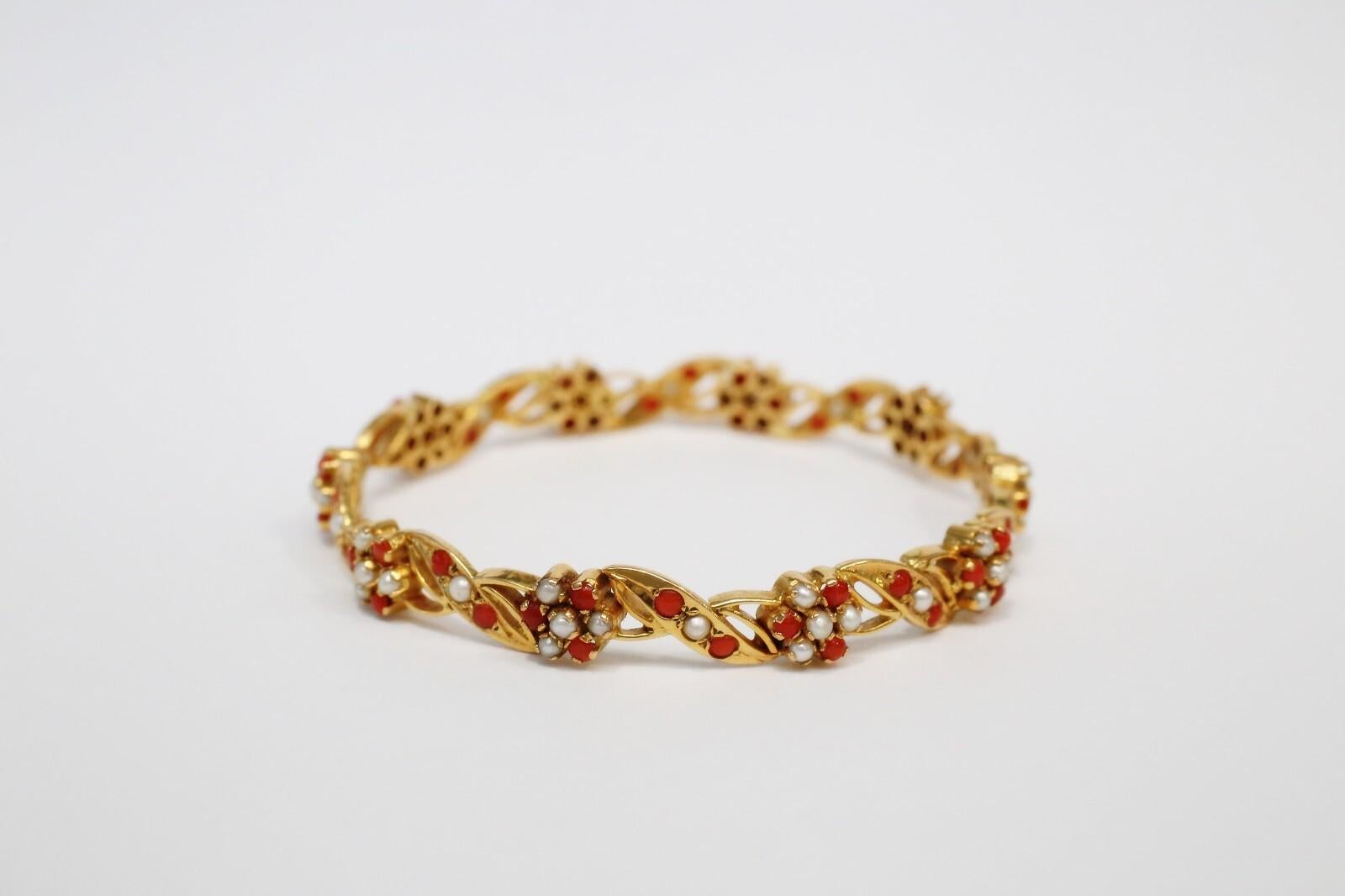 Dieser elegante Armreif aus reichem 21-karätigem Gelbgold zeigt ein kompliziertes Blumenmotiv, das mit echten Saatperlen und lebhaften Korallenperlen akzentuiert ist. Das Design wechselt zwischen gedrehten Goldgliedern und Büscheln aus roter Koralle