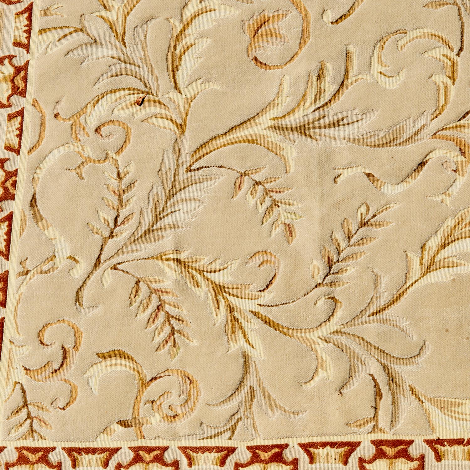 21st C. French Savonnerie style wool carpet. The design is a foliate vine pattern in gold, light green and brown tones on a cream ground. The border has a rust ground with a geometric pattern of alternating stylized wheatsheaf and leaf design.