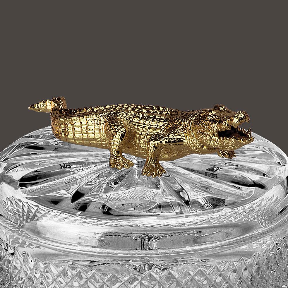 Boîte en cristal clair sculptée à la main avec Crocodrile selon la technique artisanale de la cire perdue avec finition en or patiné. Cette boîte a une forme ovale. Chaque objet est fabriqué à la main et le soin apporté à chaque détail rend chaque