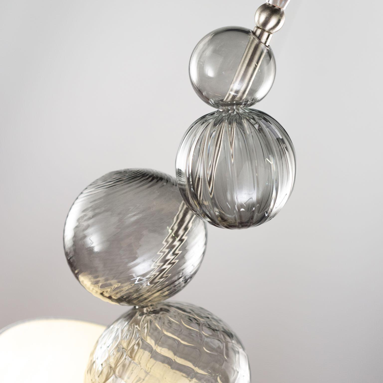 Planet è una sospensione con 1 luce dalla forma geometrica. Ha una sola luce, 4 sfere in vetro di Murano grigio, una struttura in nikel lucido e un paralume in tessuto plisse che copre la lampadina.
La particolarità di questa lampada è la texture