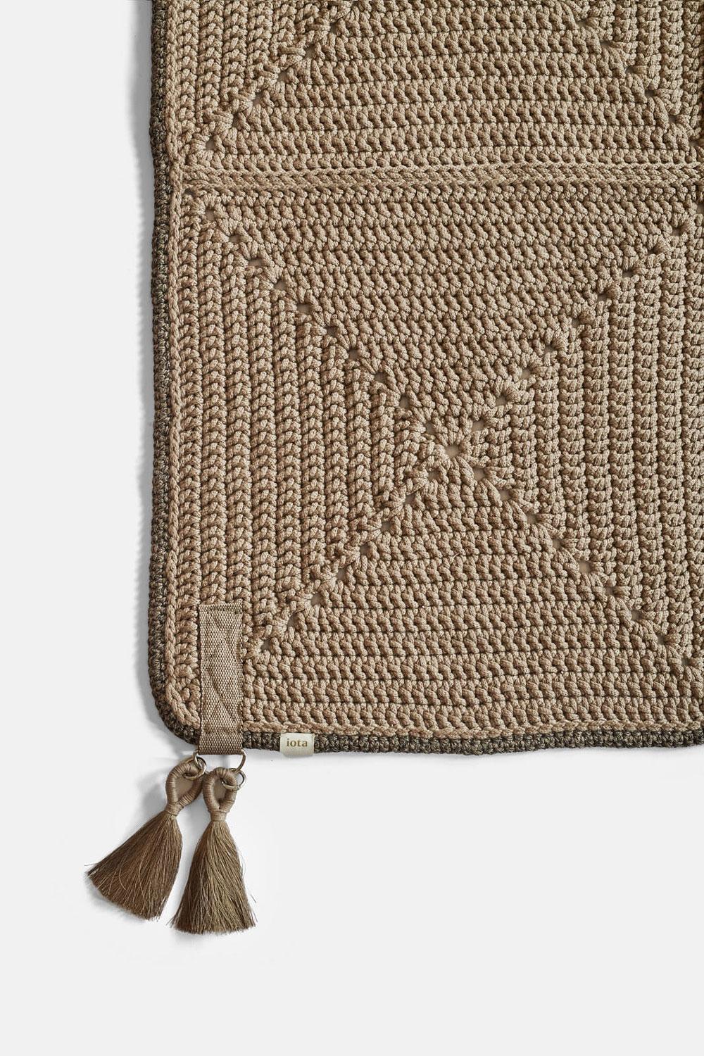 The Classic crochet granny square takes a contemporary twist in this outdoor rug. Large squares form the rug, framed with bespoke webbing. Handmade from UV protected bespoke iota yarn in earth tones, the textile is soft, yet durable and suitable for