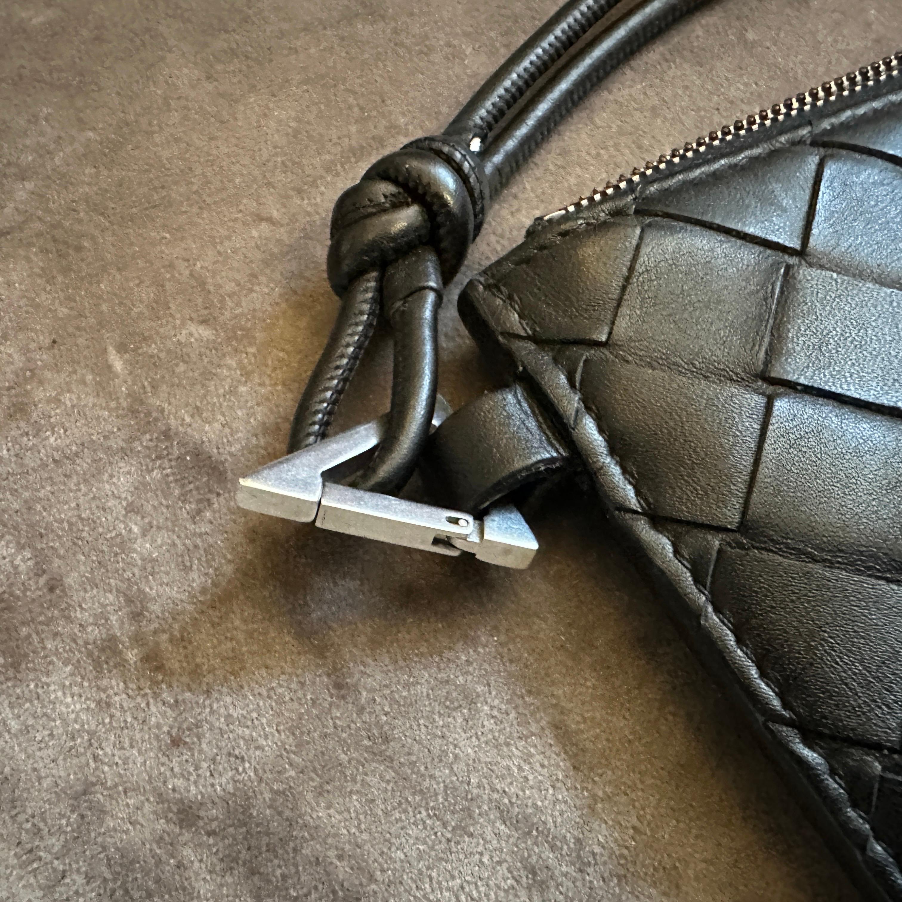 Questo sofisticato e compatto pezzo di Bottega Veneta del XXI secolo è la quintessenza dell'impegno del marchio verso il lusso tranquillo e l'impeccabile artigianato italiano. È realizzata in pelle nera, morbida e resistente, con il caratteristico