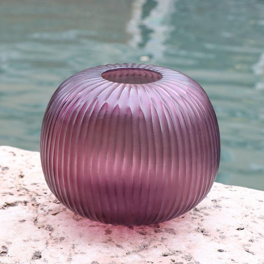 The melted glass is first blown in the heat of the furnace and shaped into a round vase with a small opening. Once solid the glass is cold carved to produce the linear cuts which mark its surface reminding us of the shell of a sea urchin,