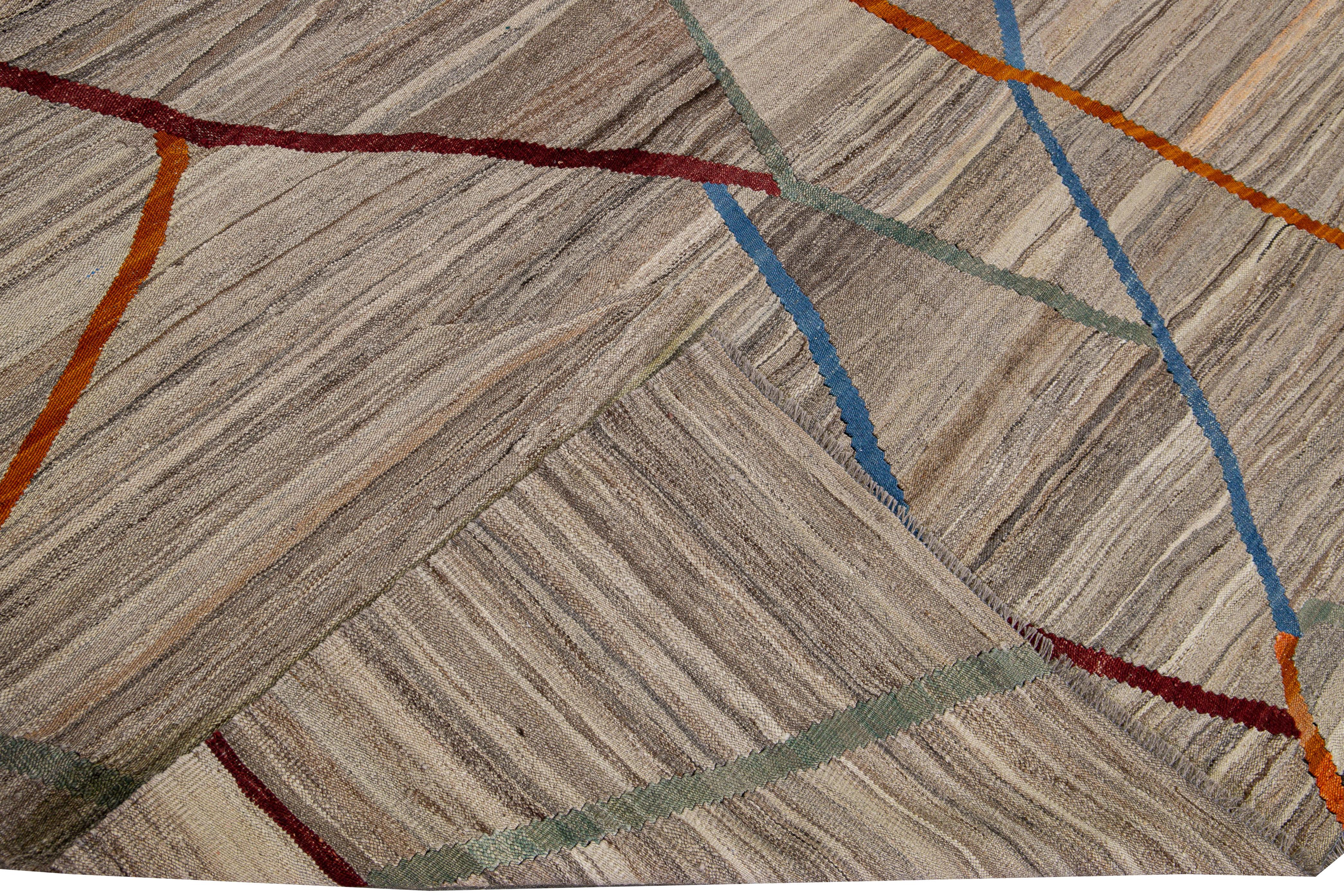 Preciosa alfombra cuadrada de lana Kilim de tejido plano moderno, anudada a mano. Esta alfombra tiene un campo de color tostado con detalles en naranja, azul y morado en un diseño geométrico.

Esta alfombra mide 9'5