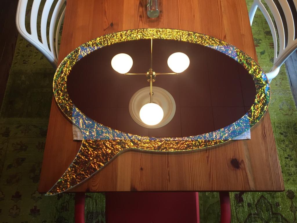 The crazy mirror is cut in the shape of a speech bubble which is familiar to anyone who has ever read comic books or animated novels. The mirror's special effect comes from a dichroic film that gives off a 3D colour-changing look. Crazy glass is