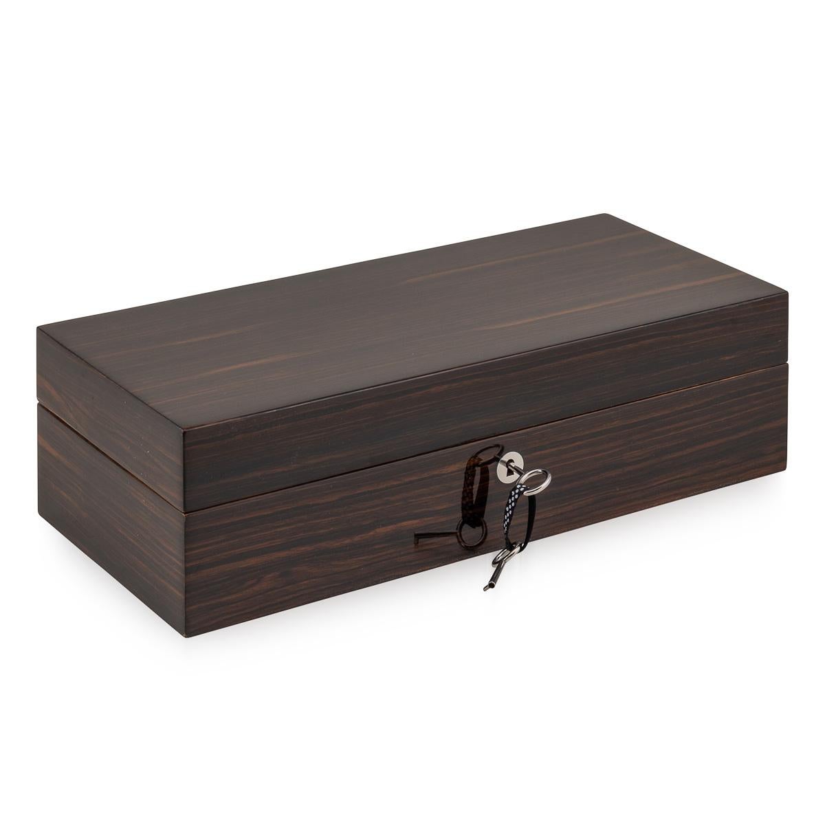 Featuring a sleek contemporary design, this watch case showcases a solid walnut carcass with stainless steel hinges & lock covered in a fine stripe macassar veneer. Upon opening, it reveals a meticulously crafted interior with four custom-made