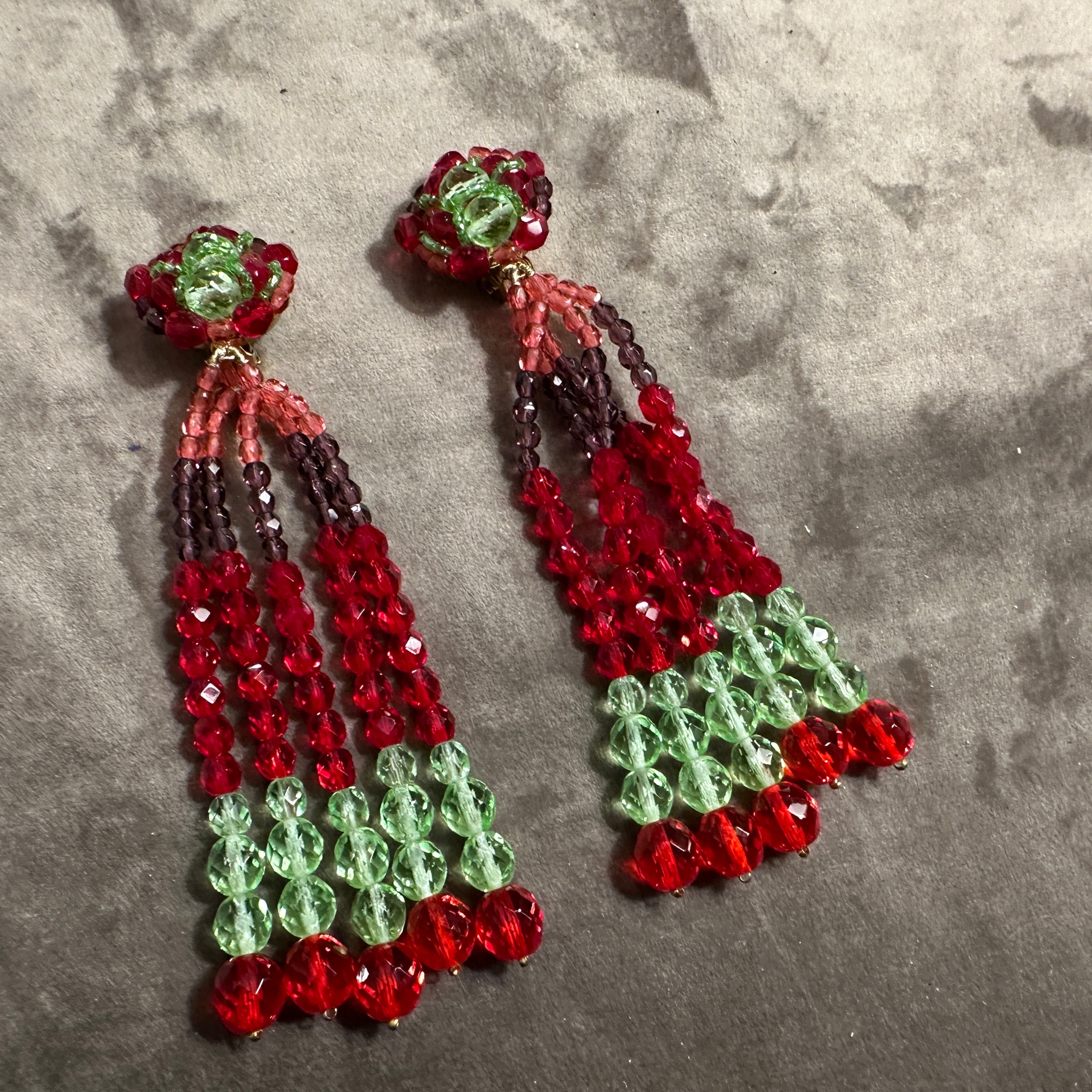 This pair of chandelier earrings is designed by Coppola e Toppo, renowned for their unique and intricate beadwork. The earrings are crafted with faceted crystal beads arranged in a stunning color combination of deep red and light lime green. Each