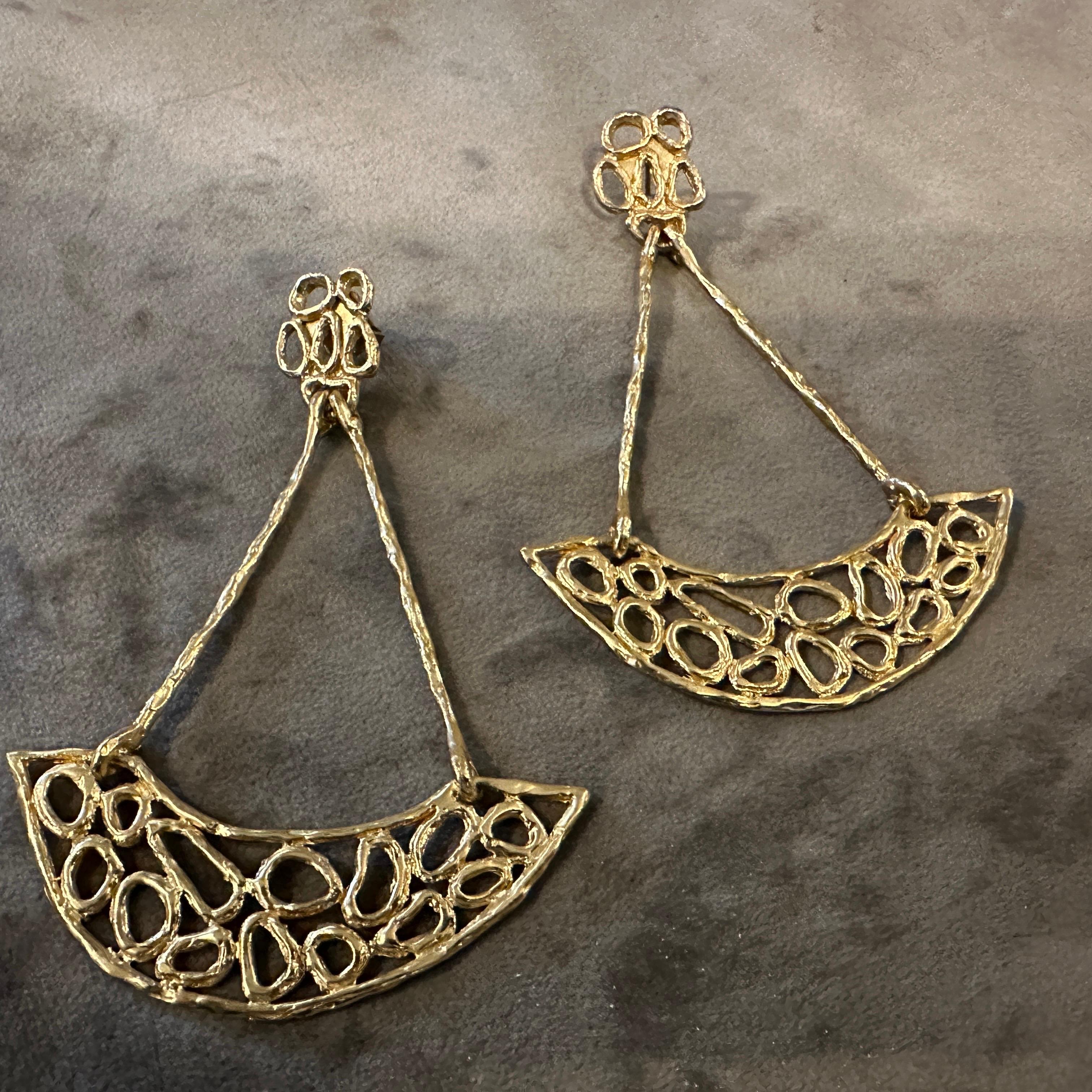 These elegant Italian costume jewelry earrings are a striking example of modern design, likely from the early 21st century. Crafted from gilded metal, the earrings feature a bold, sculptural silhouette. Each earring consists of an intricate,