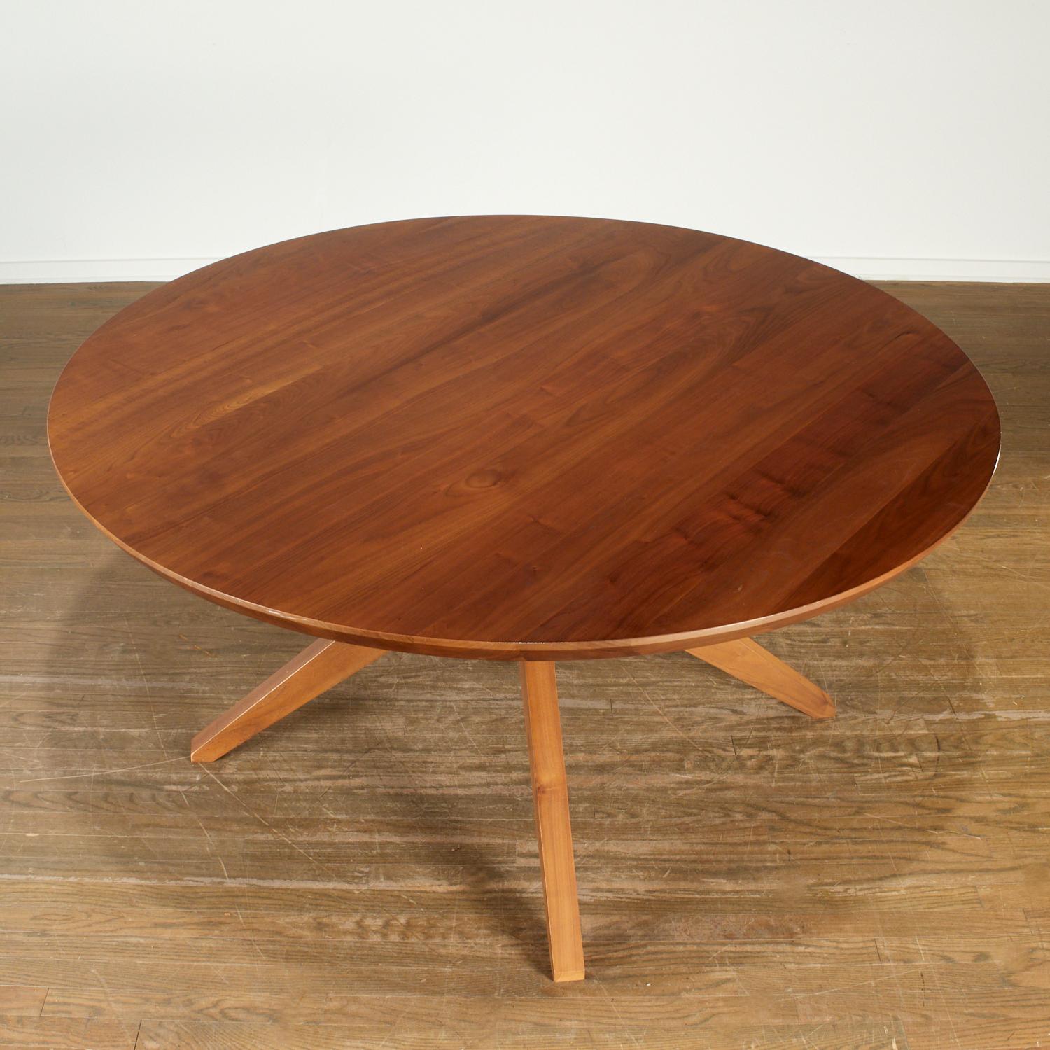 21st c., English design, solid walnut dining table, label to underside, The Cross Round Table by Matthew Hilton combines comfort with functionality while creating a contemporary piece of furniture. 

The chamfered edge detail gives a lightweight