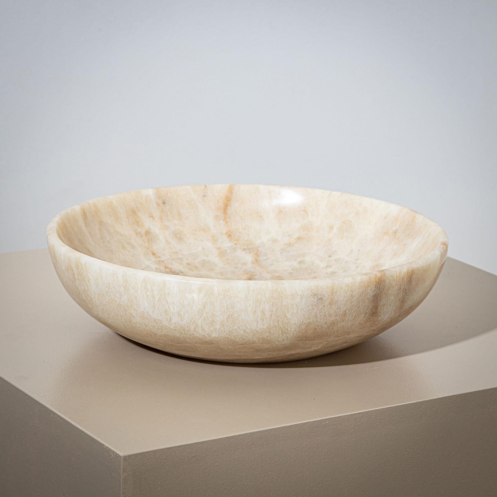 Una grande e pesante ciotola in pietra di onice beige, progettata in stile minimalista. La ciotola si distingue per il bordo dolcemente inclinato e la forma piatta e armoniosa, che trasmette un'eleganza senza tempo.