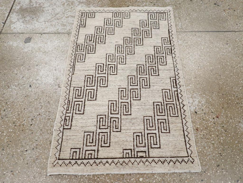 Une pile de laine composée de nœuds asymétriques sur une base de coton. Quatre diagonales de frettes brunes quadrillées parcourent le champ de paille sablonneux de ce tapis de ville oasis miniature. Bordure écru paille avec une ligne en zig