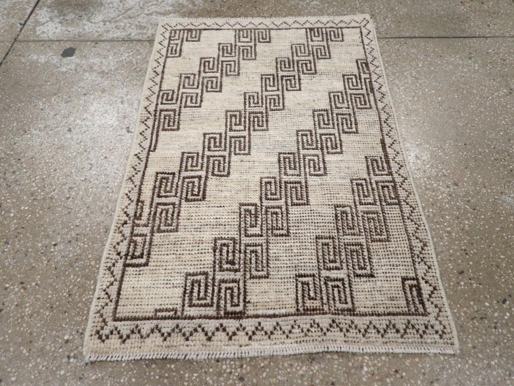 Un mucchio di lana con nodi asimmetrici su una base di cotone. Forse uno dei Khotan più piccoli in assoluto, con un disegno a spirale quadrata diagonale e ripetuta in marrone scuro su paglia sabbiosa. Bordo principale in paglia sabbiosa a Zig