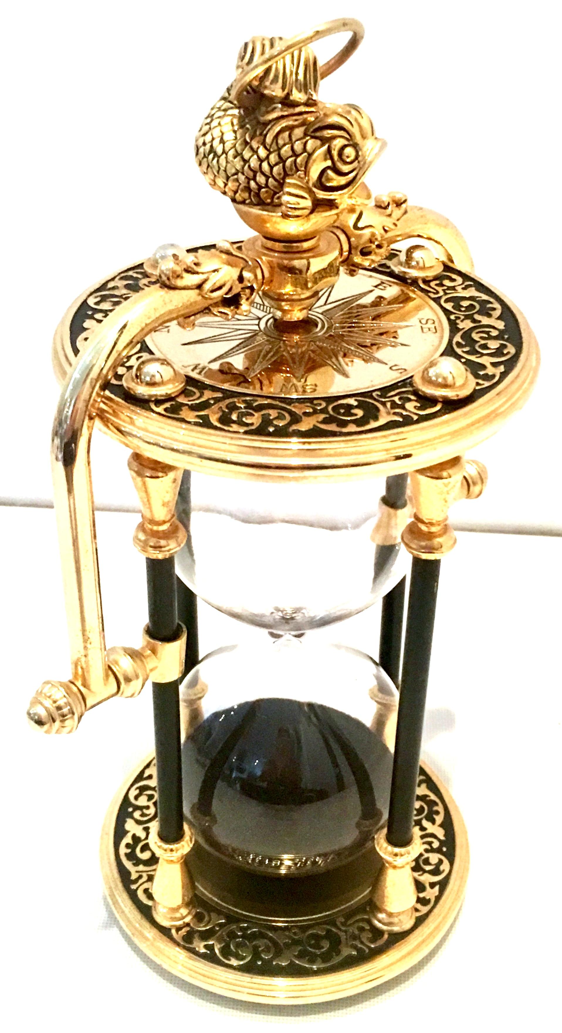 21st century gilt gold brass, black enamel & blown glass hanging hour glass. Features, black sand, a Koi fish detail where the loop hook is for hanging, raised gold over black enamel scroll motif and each end has an etched decorative compass.
Can