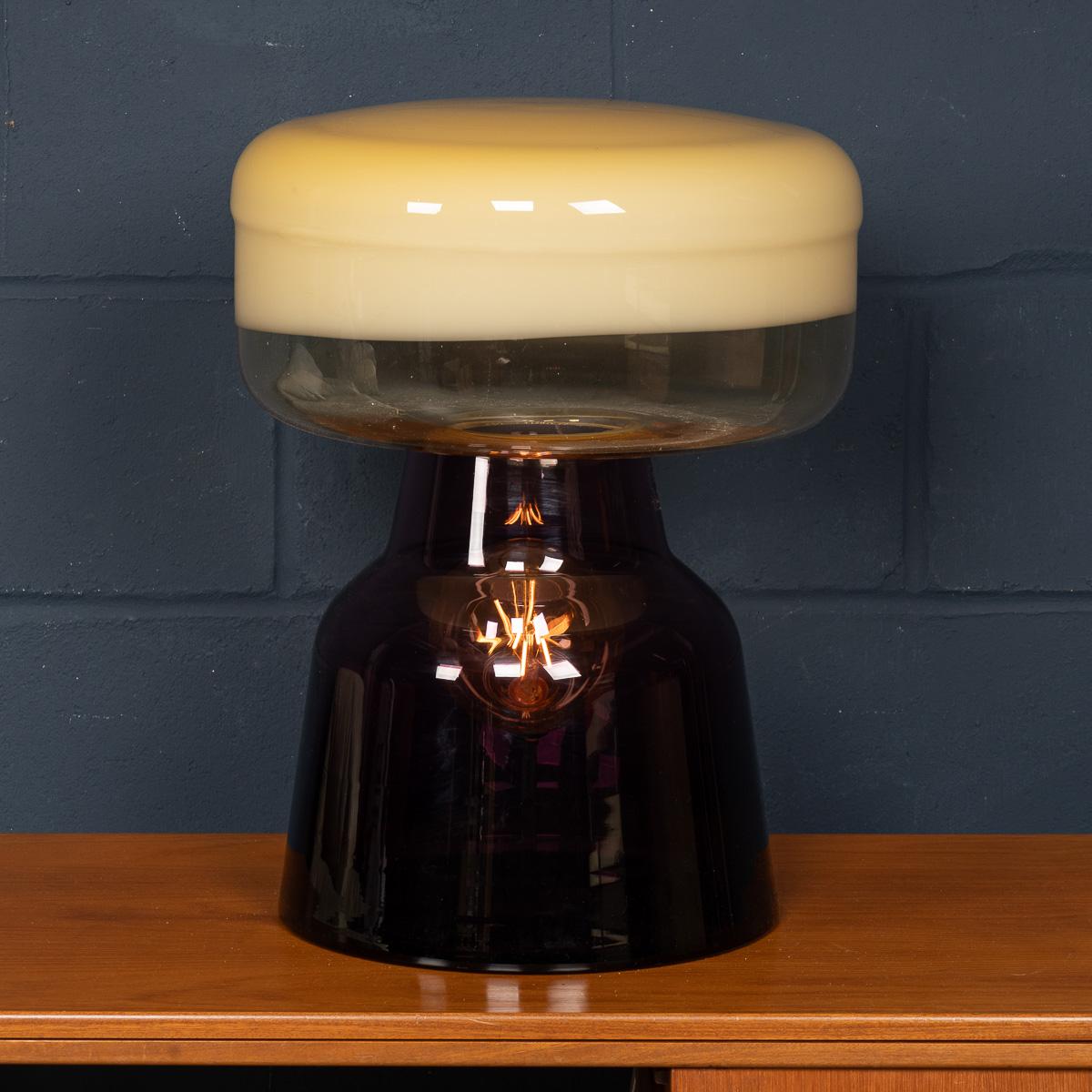 Cette lampe sculpturale en verre soufflé à la main, fabriquée à Murano, Venise, Italie, est un exemple étonnant de design contemporain. La lampe présente une composition empilée de deux éléments distincts : une base ambrée supportant un abat-jour