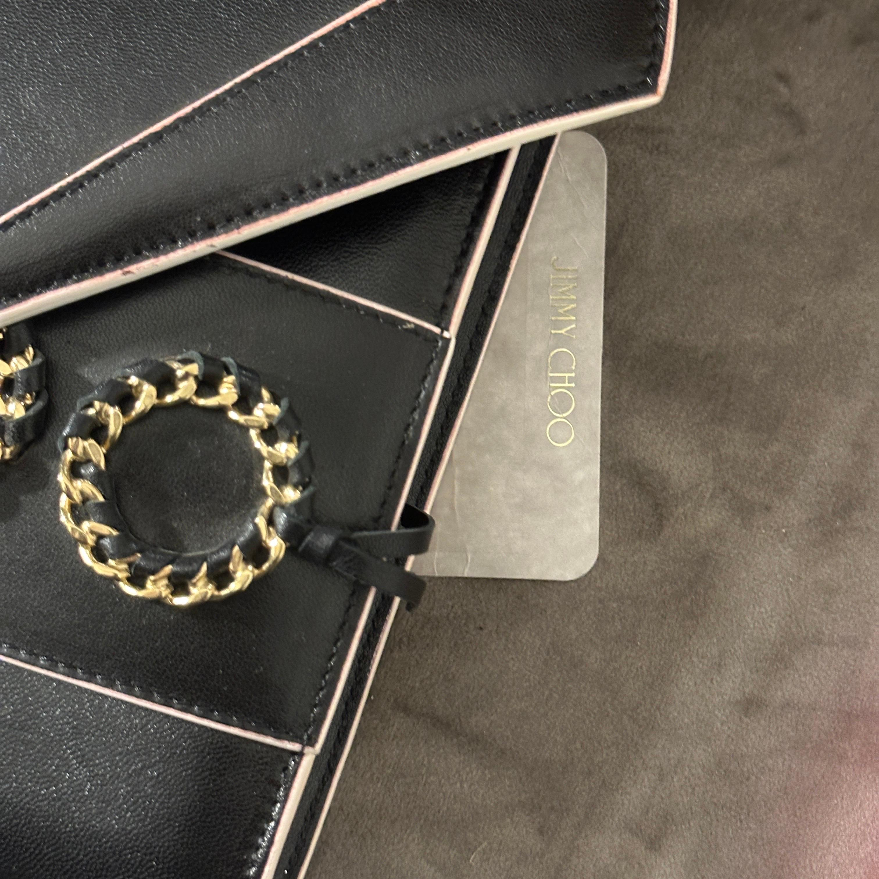 This 21st-century Jimmy Choo crossbody bag is a striking example of modern luxury, blending minimalist design with bold branding and edgy details. Made from smooth black leather, the bag features a structured geometric silhouette, highlighted by