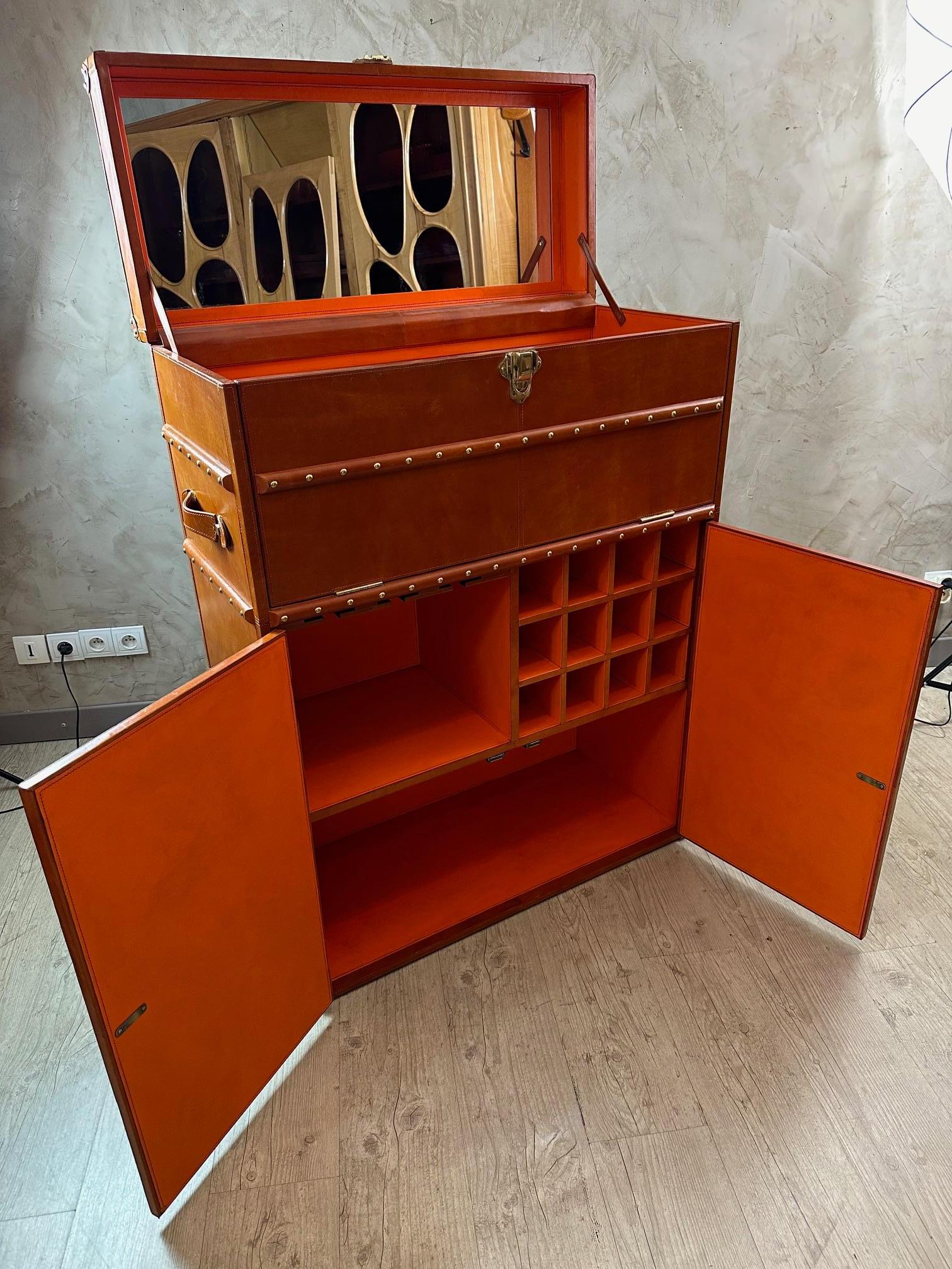Exceptional bar trunk made in leather and brass fittings opening from the top hiding a mirror.
The upper part lowers to become a tray for making cocktails.
The lower part is composed of two hinged doors and compartments used to store stemmed