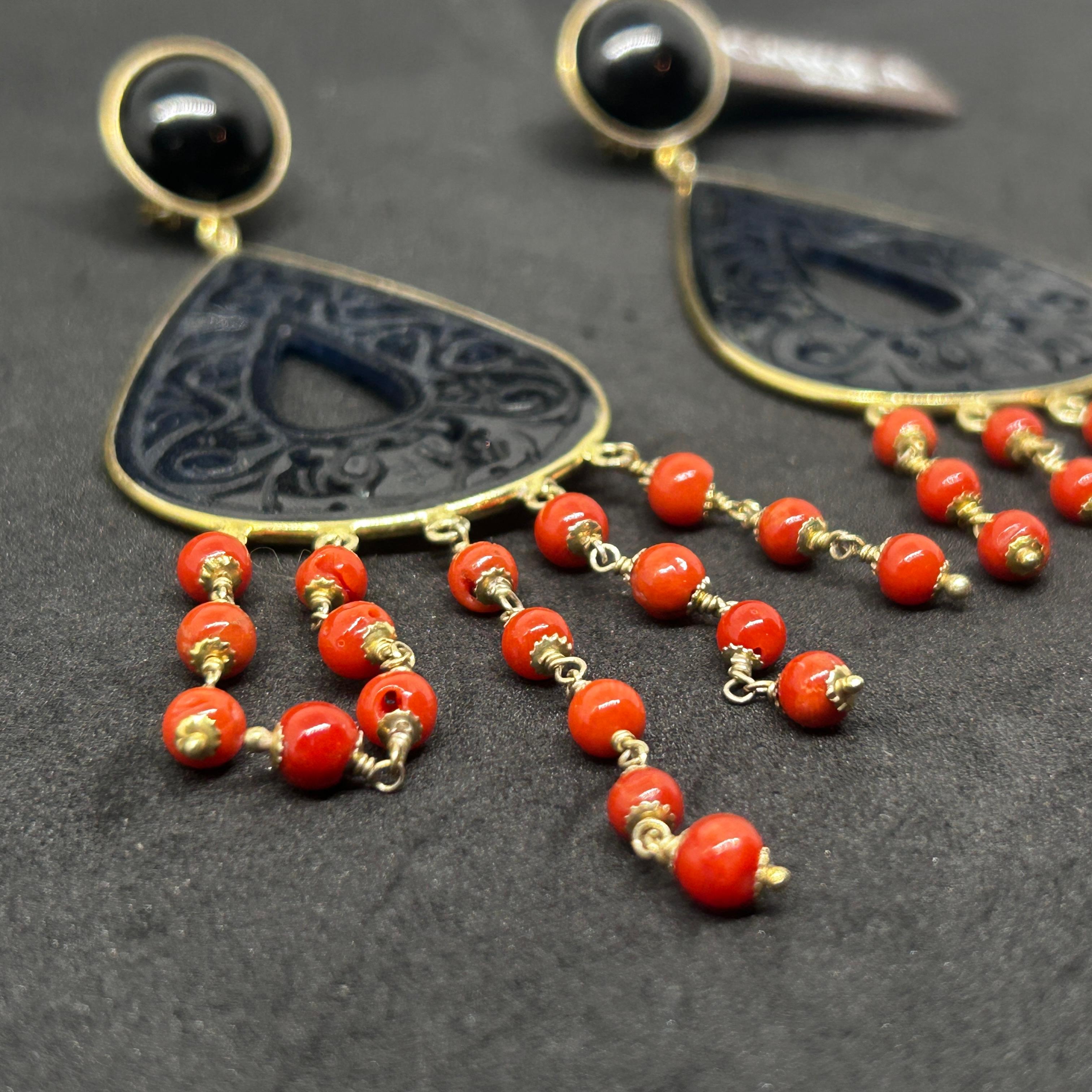 These earrings are a pair of 21st-century Mediterranean-inspired chandelier earrings by the designer Carola. They combine black onyx and vibrant coral beads in an elegant and eye-catching design. The earrings feature a teardrop-shaped onyx piece