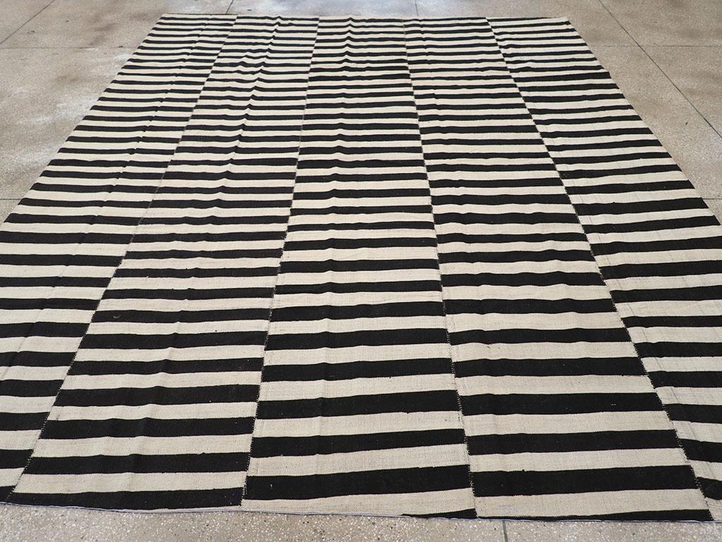 Esta alfombra Kilim Persa de Tejido Plano del siglo XXI, que mide 30 cm x 30 cm, presenta un atrevido diseño a rayas negras y marfil que destaca tanto la sencillez como la artesanía. Las rayas alternas se disponen en paneles verticales, cada uno con