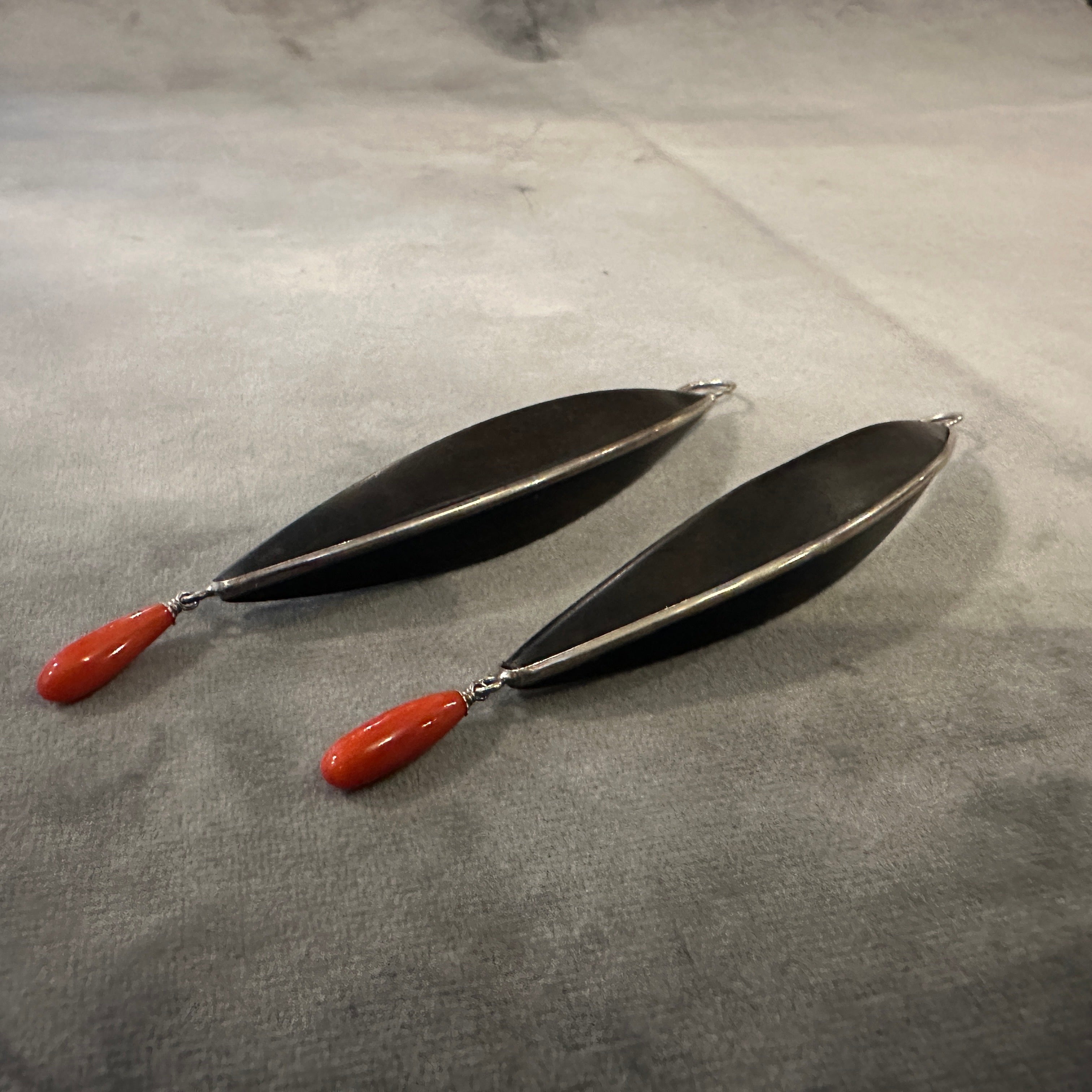 These earrings are striking examples of 21st-century modern design, blending organic and minimalist aesthetics with bold materials. The earrings feature a long, elegant curve, reminiscent of a stylized leaf or pod, giving them a fluid, sculptural