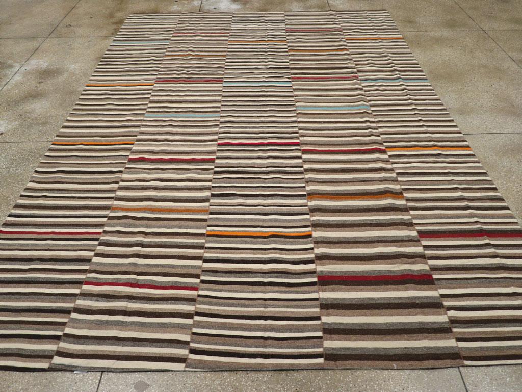 Esta alfombra turca Flatweave Kilim del siglo XXI, que mide 3,9 m x 4,8 m, presenta un dinámico diseño de rayas horizontales dispuestas en distintos paneles verticales. La paleta terrosa se acentúa con sutiles estallidos de color, como el rojo
