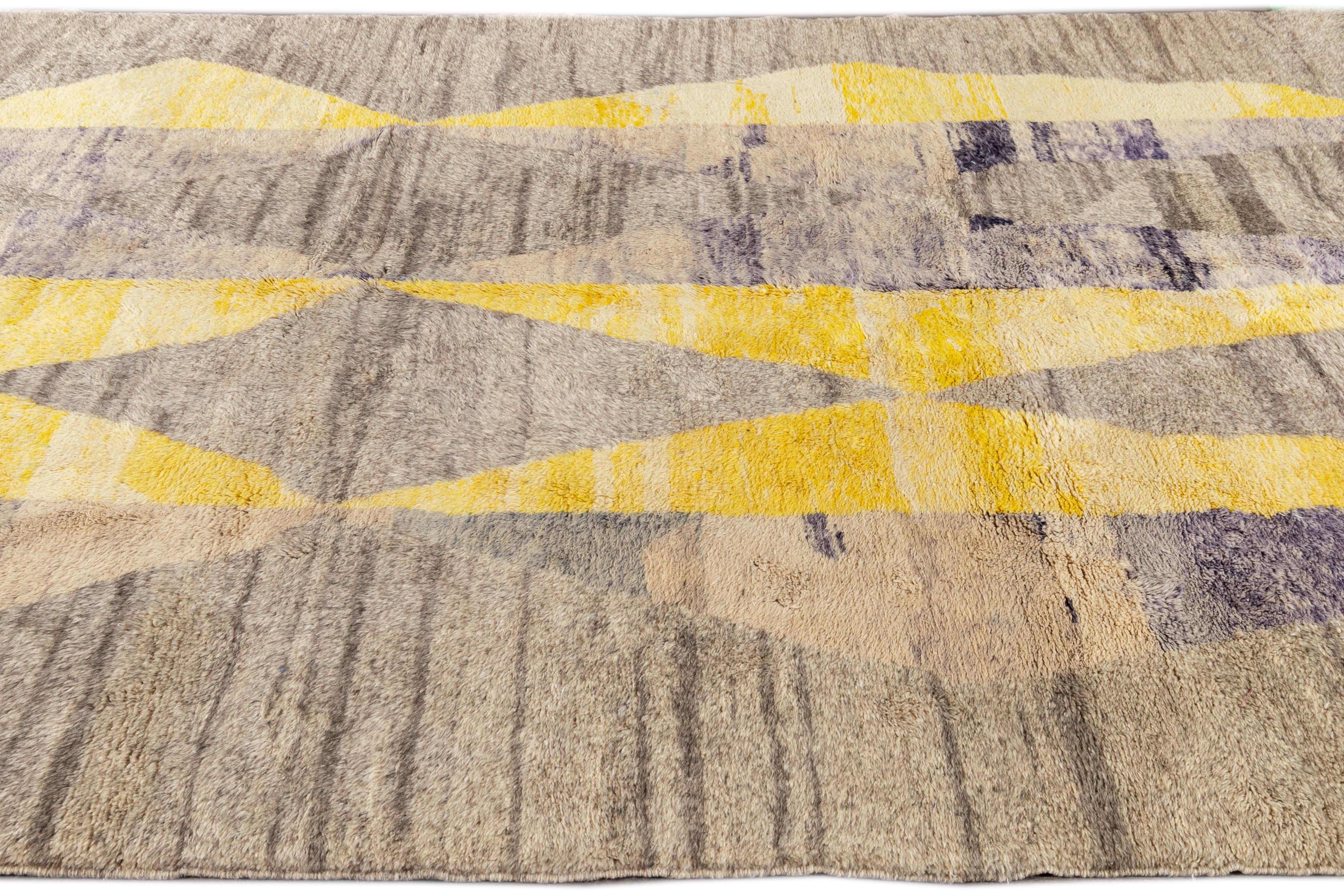 Dieser zeitgenössische marokkanische Teppich aus dem 21. Jahrhundert zeichnet sich durch ein neutrales hellbraunes/graues Feld und abstrakte geometrische Muster mit blau-violetten und gelben Akzenten aus.

Dieser Teppich misst: 7'9' x 10'7