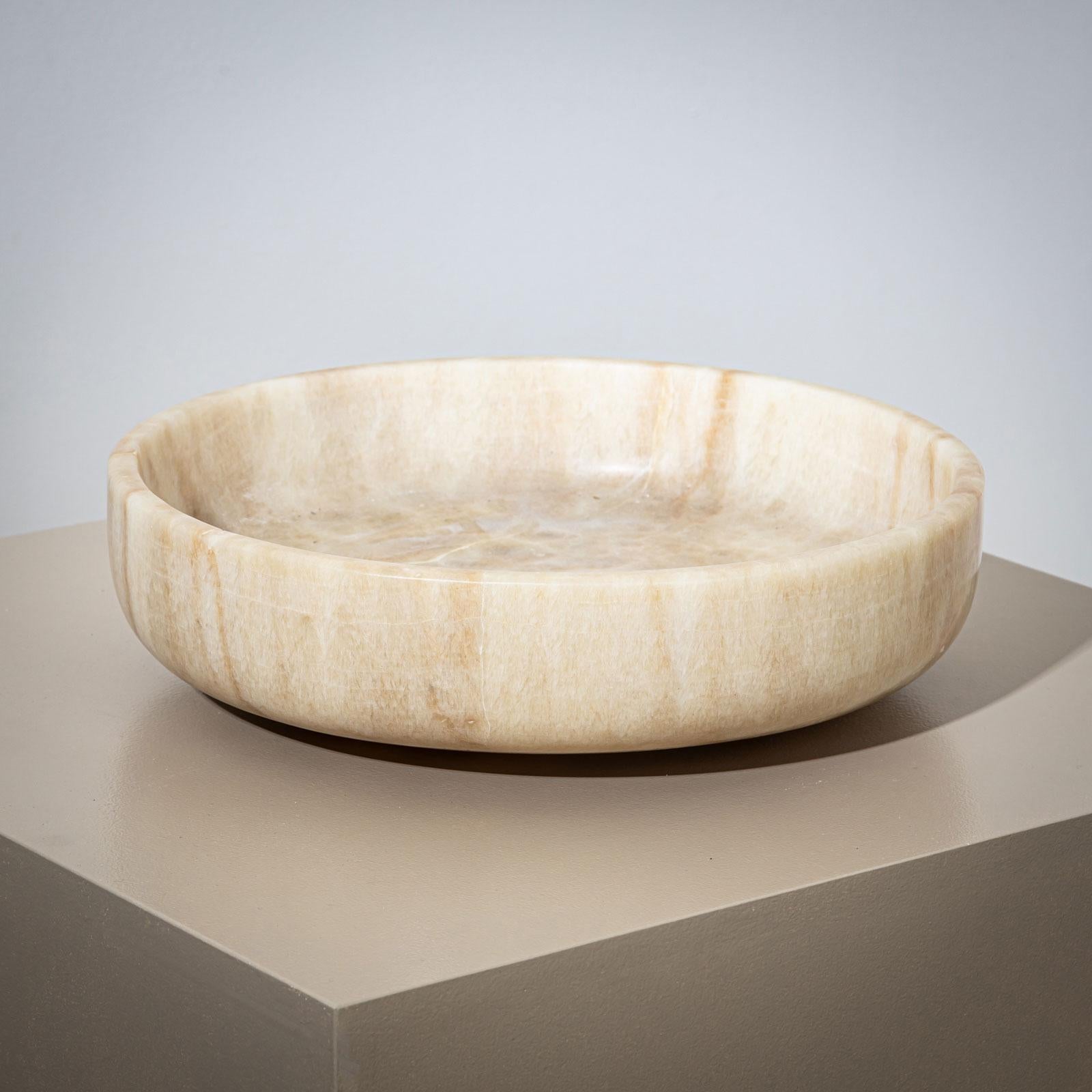 Una grande ciotola in pietra realizzata in onice beige, dal design minimalista. La ciotola è caratterizzata da un bordo alto e da una forma piatta. È stato riparato una volta, anche se questo non toglie nulla alla sua sobria eleganza. 