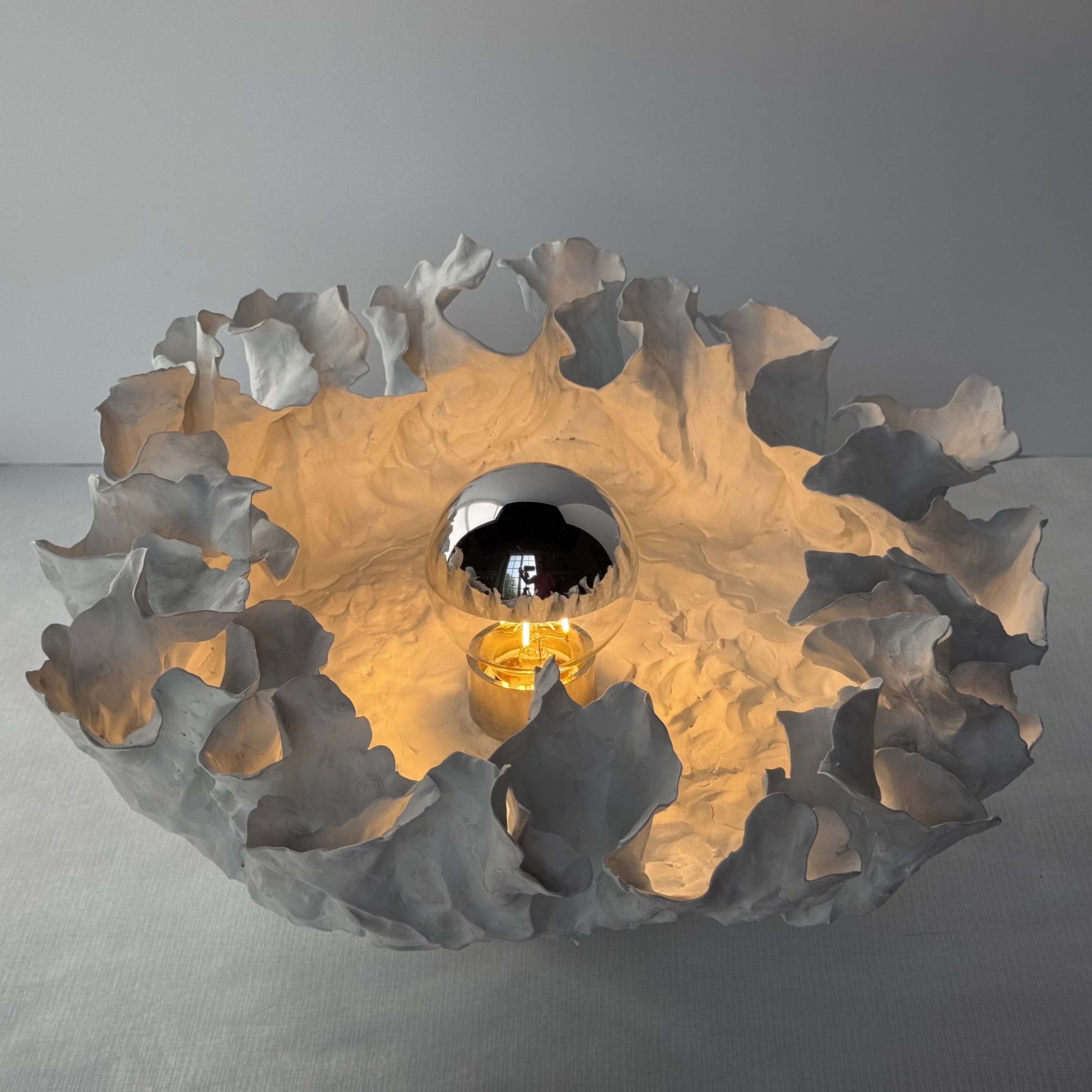 Hand built porcelain table lamp by American artist Charles Burleigh.

This work, bisque fired and unglazed, renders a striking translucent effect when illuminated from behind the surface of the lamp. The surface is activated by the hand formed clay,