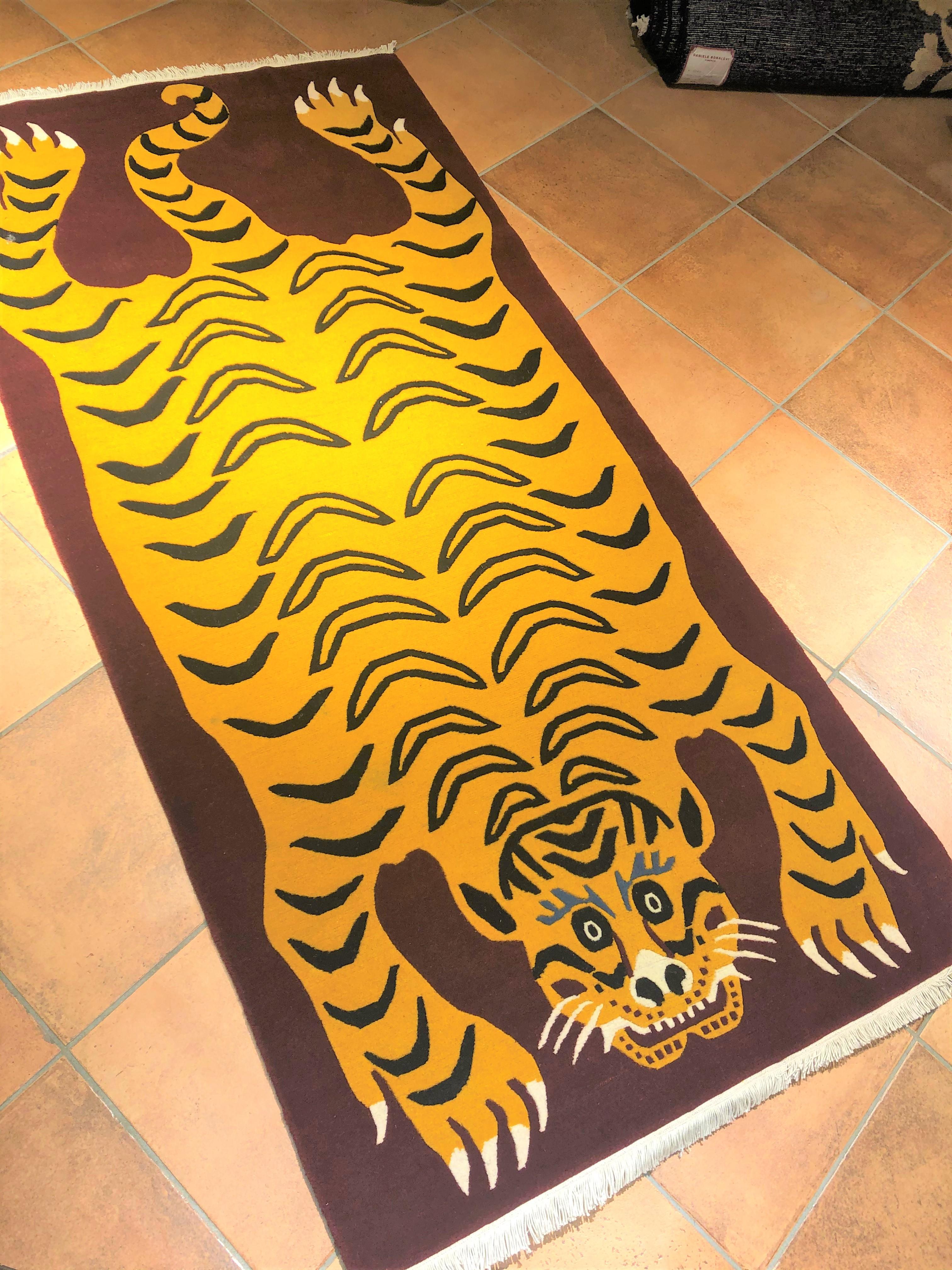Teppich aus nepalesischer Produktion, geknüpft aus handgesponnener Wolle mit tibetischem Knoten. Der Hintergrund ist purpurrot und der Rücken des dargestellten Tigers ist reich mit dem traditionellen gelben Fell dieser Raubkatzen verziert. Das