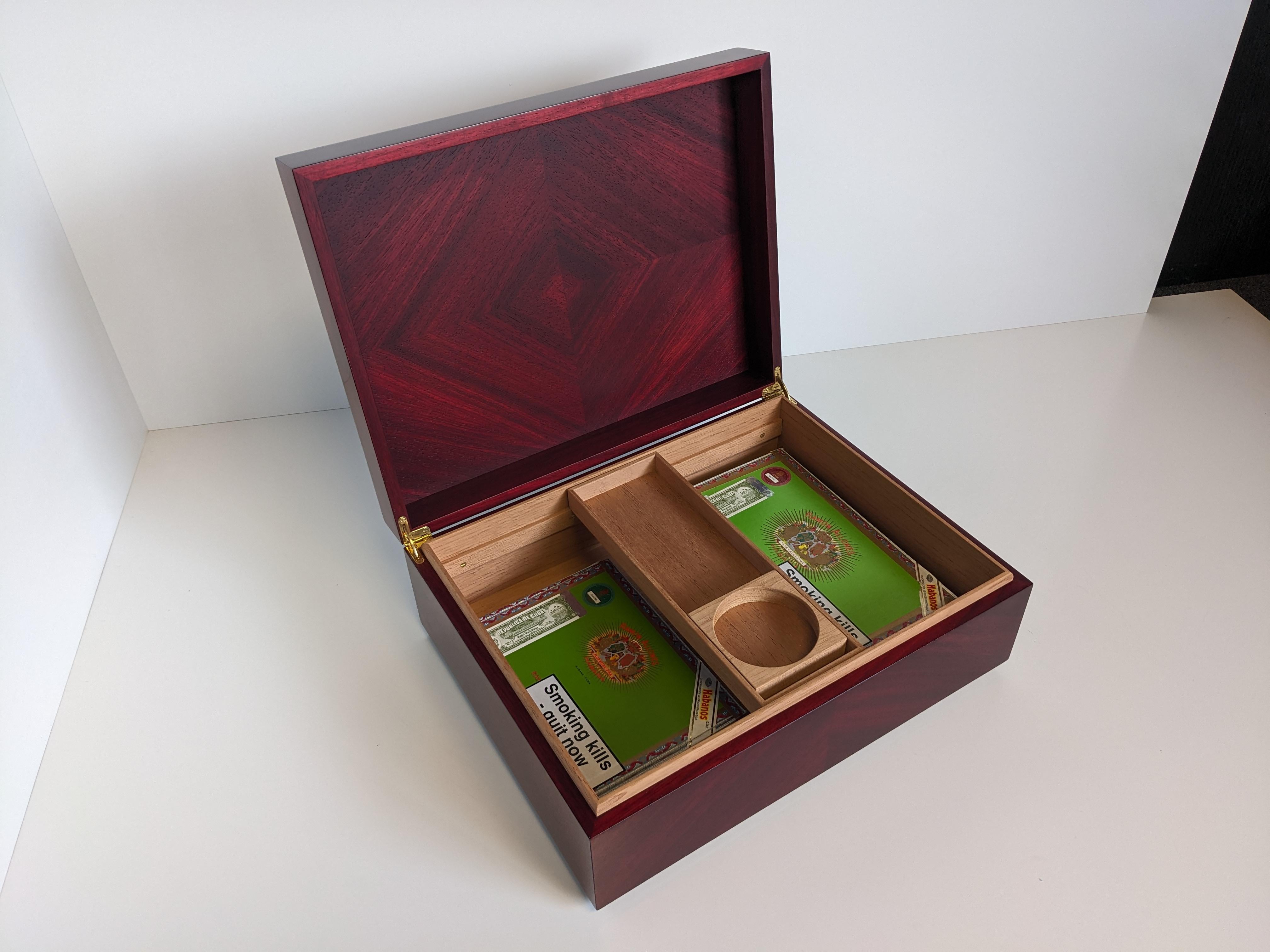 Luxurious humidor made in Red stained Padauk veneer, with solid cedar lining. The veneers are laid in a quartered diamond pattern. The ovolo moulded edges are ebonised and the whole outside is finished with a gloss lacquer.
The hinges are solid