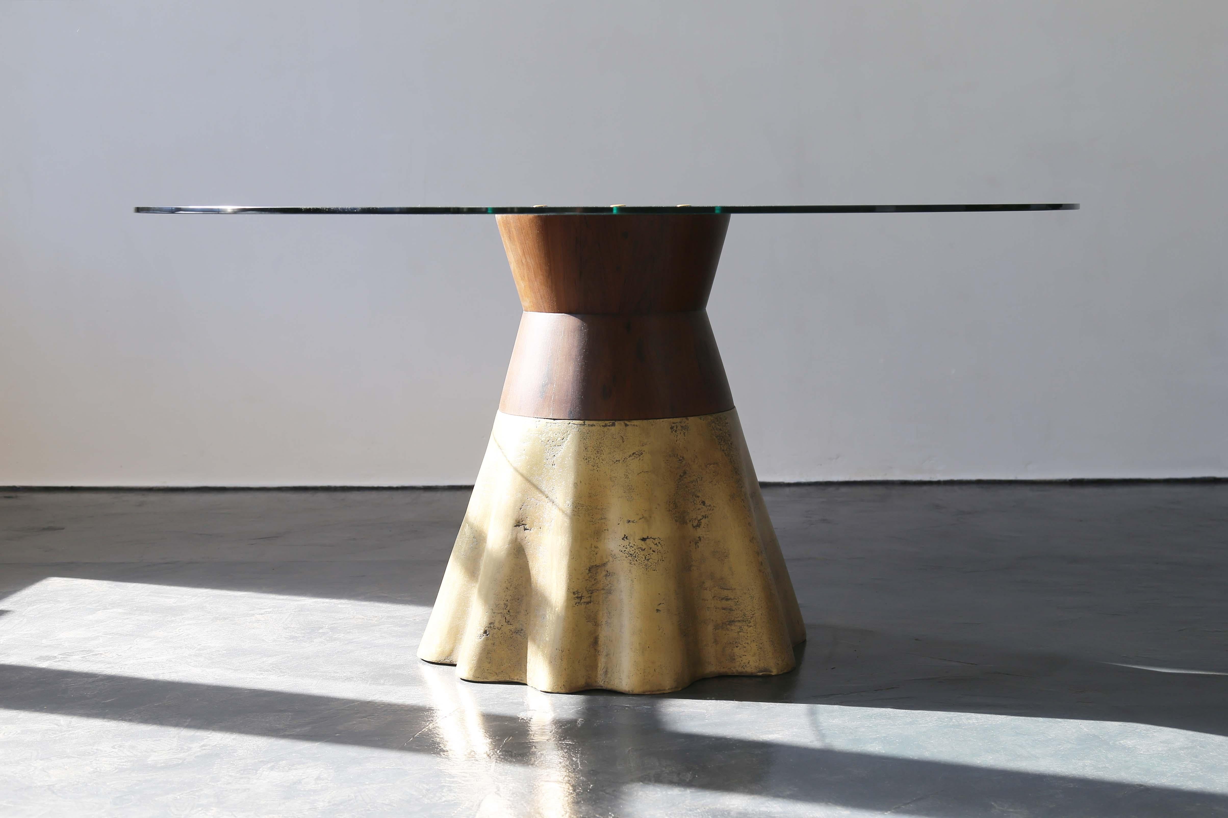 The Tavola 9 features a seemingly organic, wavy cast bronze base joined to a rigid, conical wood support and shown here with a glass top.  Only partially polished to show the evidence of the burnt earth that once surrounded the bronze, no two bases