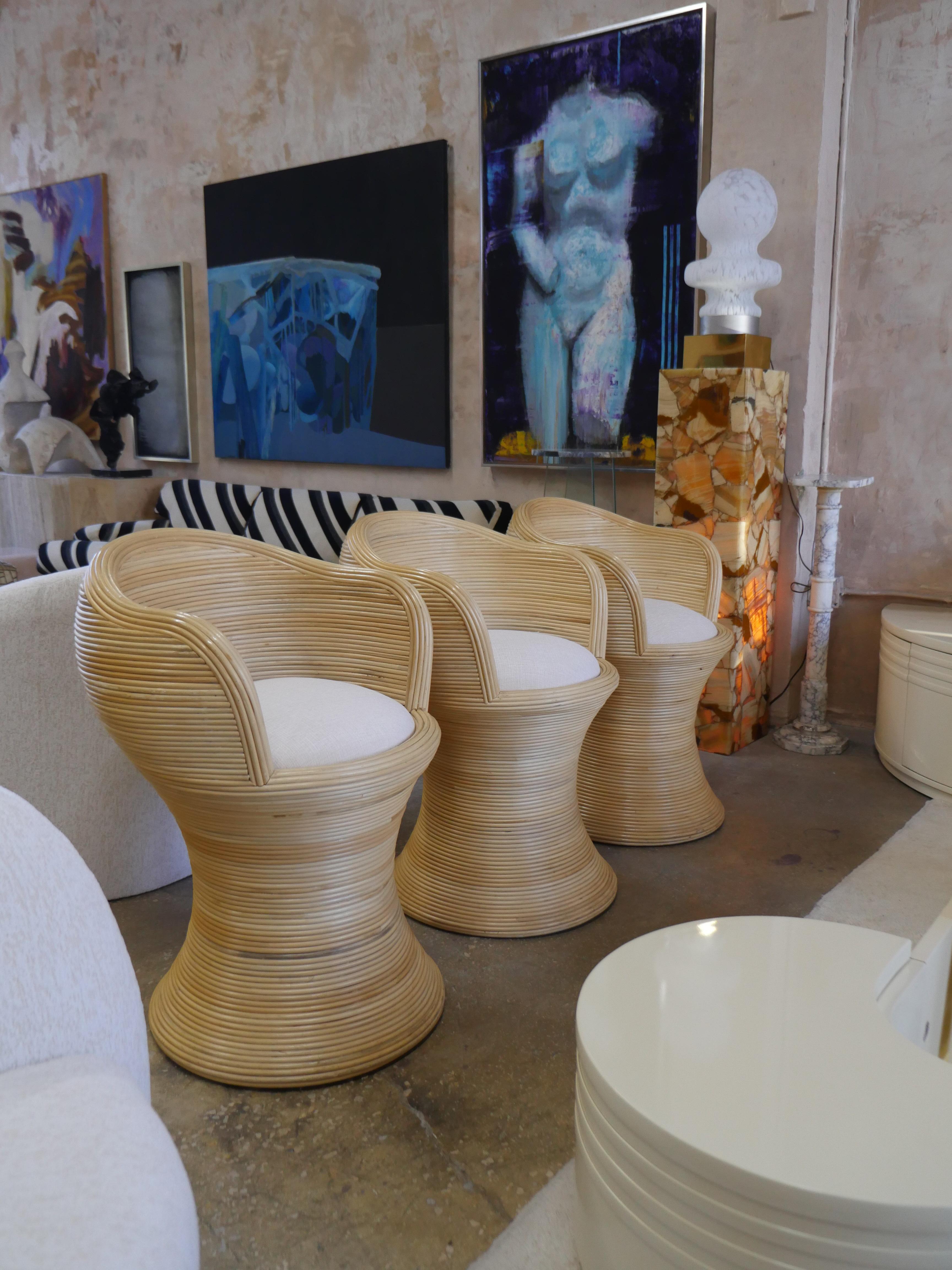 Stunning set of three Palm Beach modern pencil reed rattan stools. Their sleek, sculptural design is perfectly complemented by luxurious off-white chenille upholstery from renowned designer Holly Hunt. Whether you're styling a chic kitchen island or