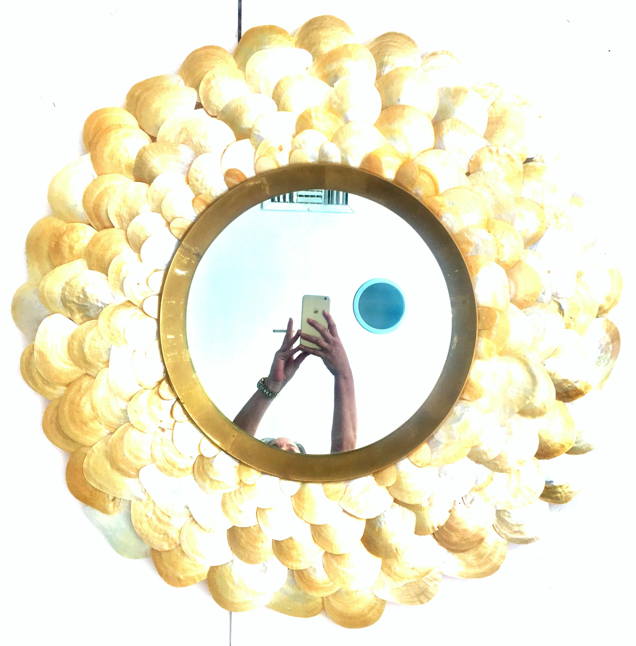 21st century sea shell and brass round convex hanging wall mirror. This dramatic substantial and classic piece of art features lacquered sea shells in a golden hue surrounding a solid brass framed convex mirror. The solid brass framed convex mirror