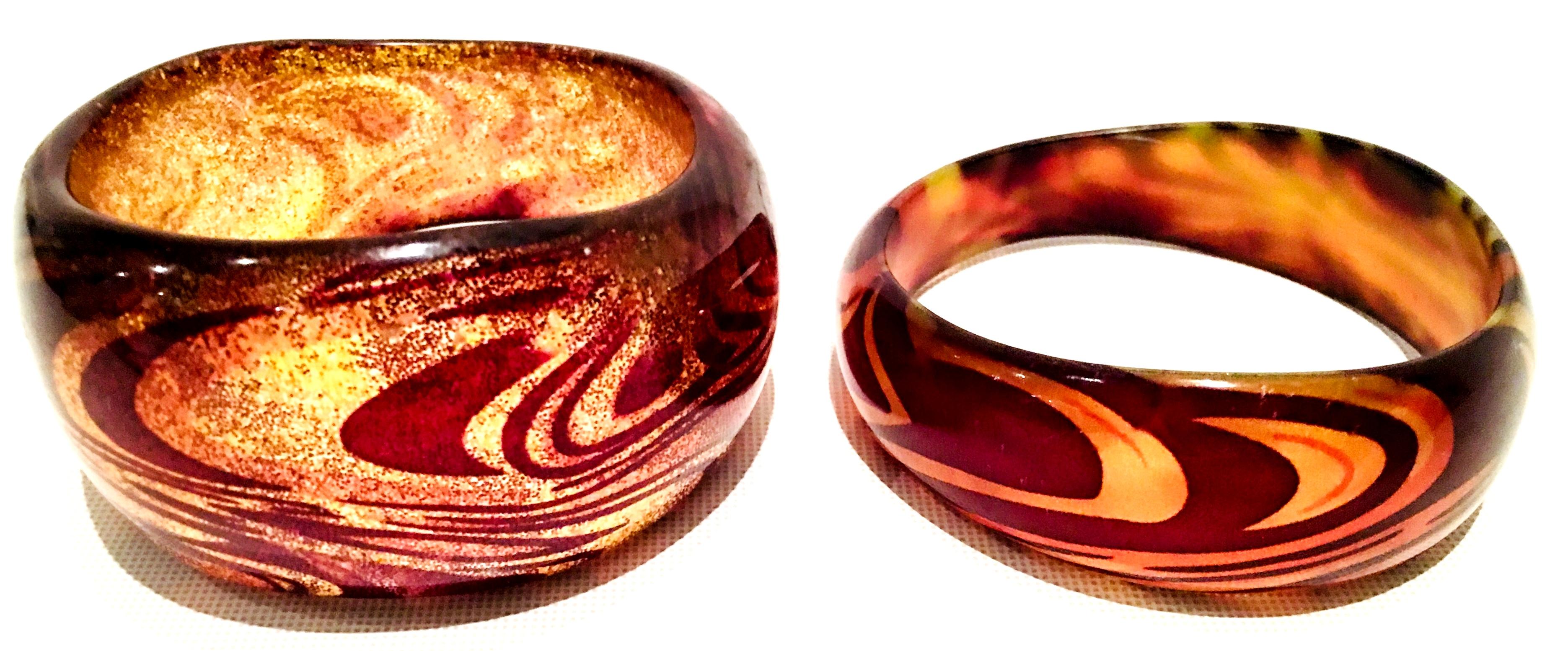 21st Century Set Of Two Lucite Metallic Feather Print Bangle. This Set of Two Metallic Feather Print Bangle Bracelets features a warm palette of amber, brown and gold. The 2 piece set includes two different size bangle bracelet
smaller bangle
