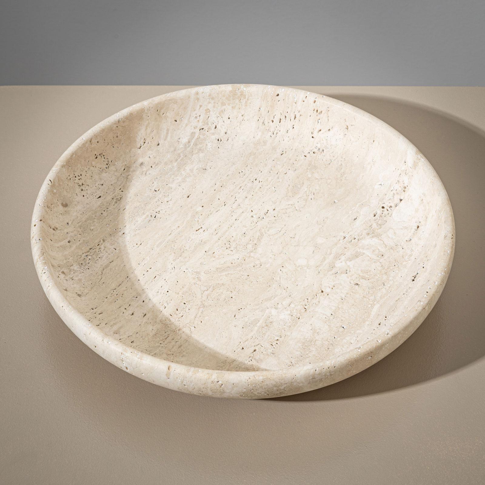 Un grand bol en pierre lourde, fabriqué en travertin beige, au design minimaliste. Son bord légèrement incliné et sa forme plate confèrent au bol une élégance harmonieuse et intemporelle.