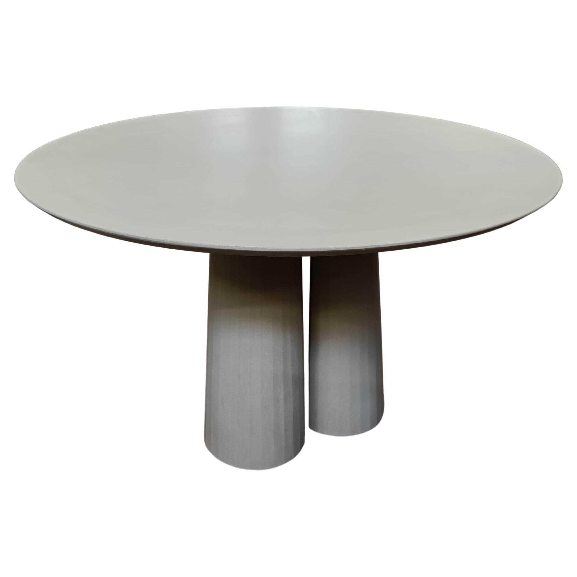 Table de salle à manger de forme arrondie faisant partie d'une collection de système modulaire en mortier de ciment ultra performant. Plateau et base en UHPC colorés dans le mélange et sablés. Disponible en huit couleurs différentes : Brick, silver,