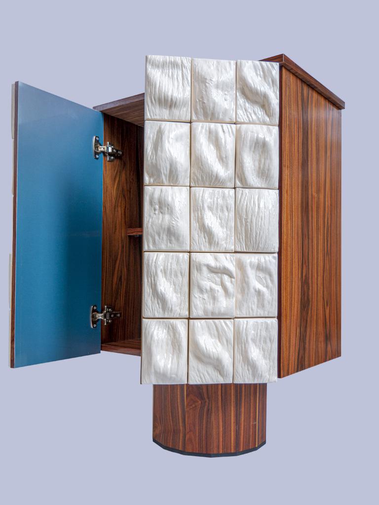 Handmade ceramic and walnut wood cabinet by Rem Atelier 

Surface cabinet
The clad cabinet combines different material characteristics into a functional sculpture. Thirty ceramic tiles shape the front surface of the cabinet, fusing into an organic