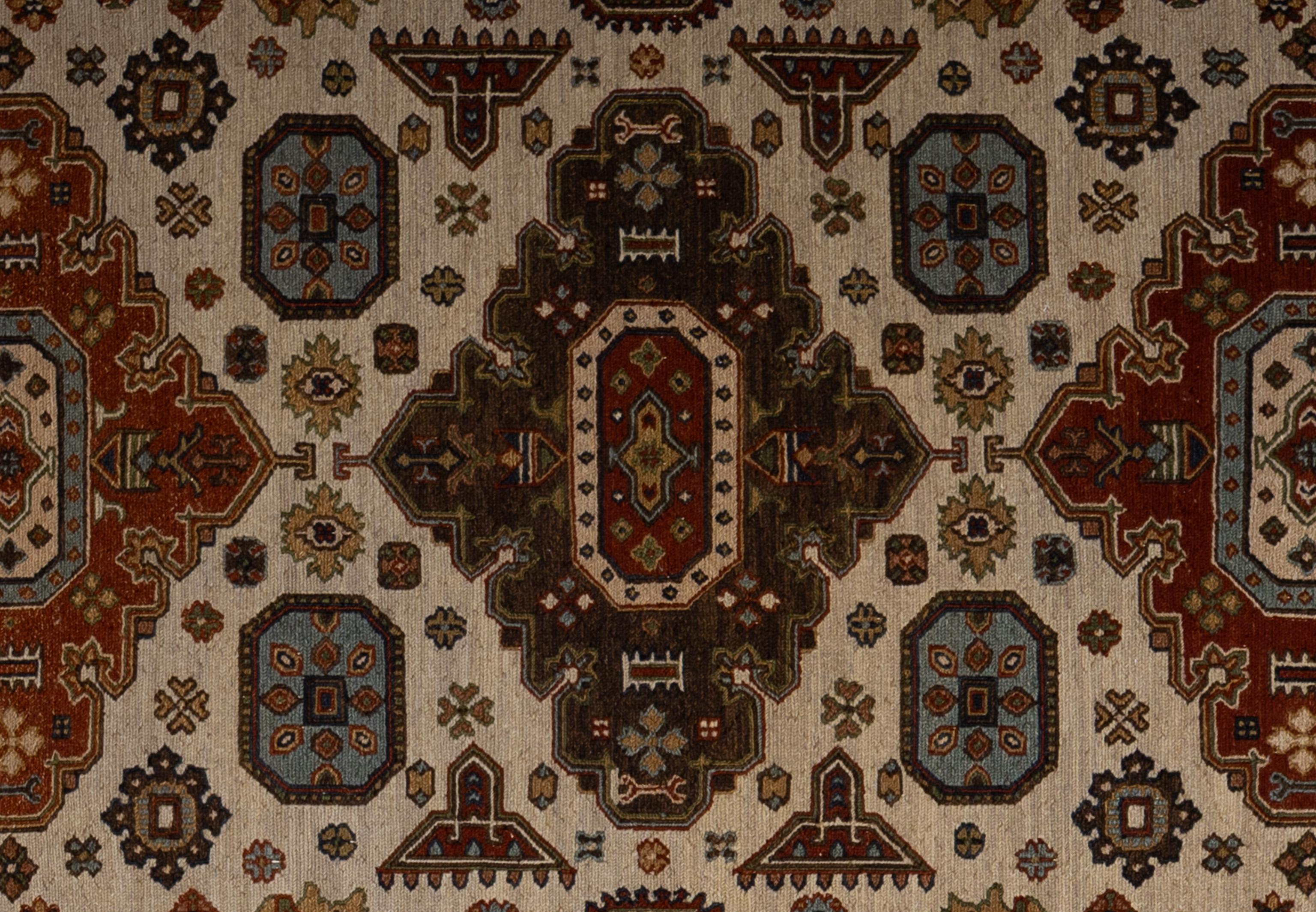 Questo tappeto indiano in stile uzbeko, tessuto a mano, mostra un disegno tribale audace e intricato, caratterizzato da ricchi toni rossi, oro, crema e blu tenue. Il layout presenta tre pannelli verticali di rilievo, ognuno dei quali è ornato da