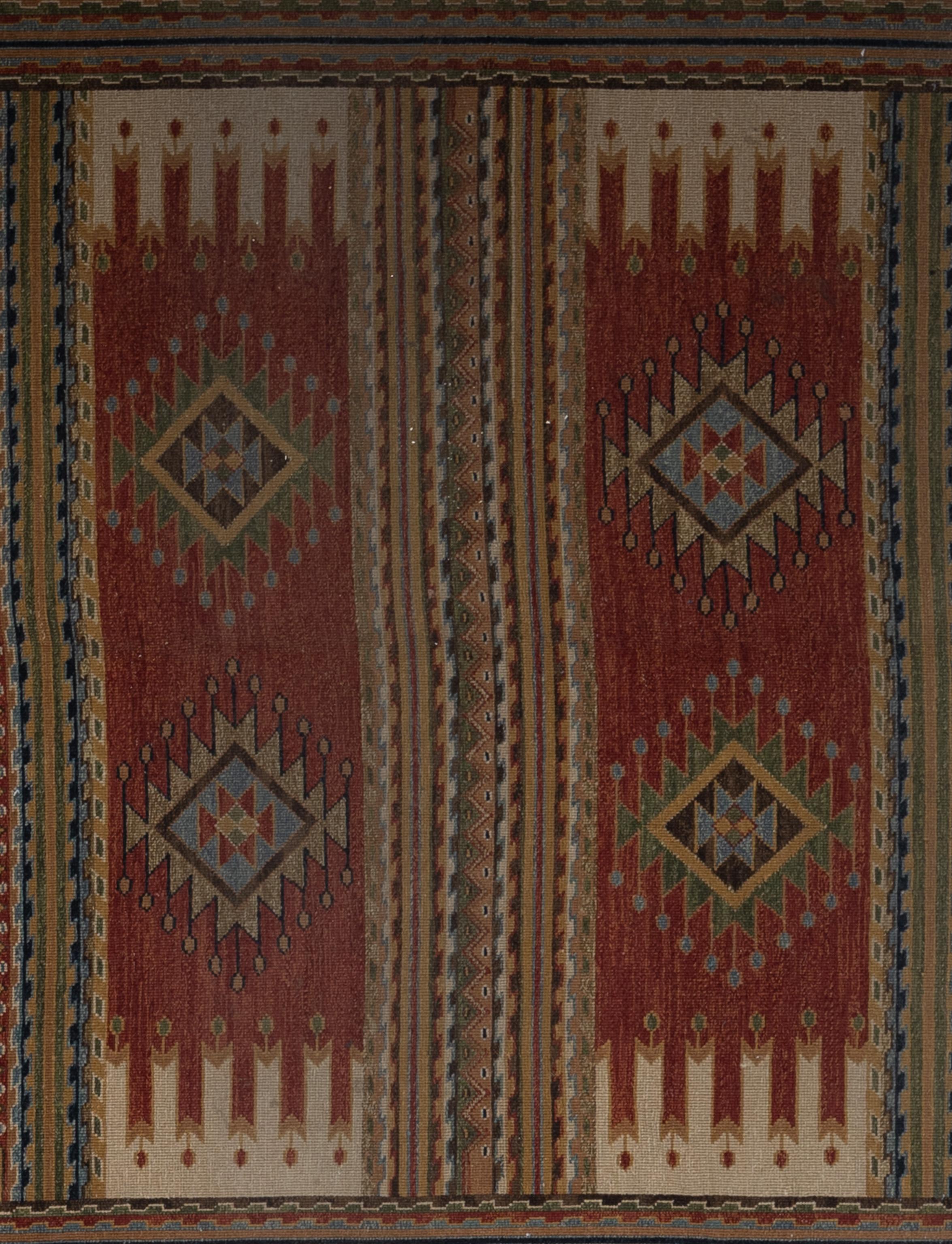Esta alfombra de estilo uzbeko, tejida a mano en la India, muestra un diseño tribal intrincado y audaz, caracterizado por ricos tonos rojos, dorados, crema y azules apagados. El diseño presenta tres prominentes paneles verticales, cada uno adornado