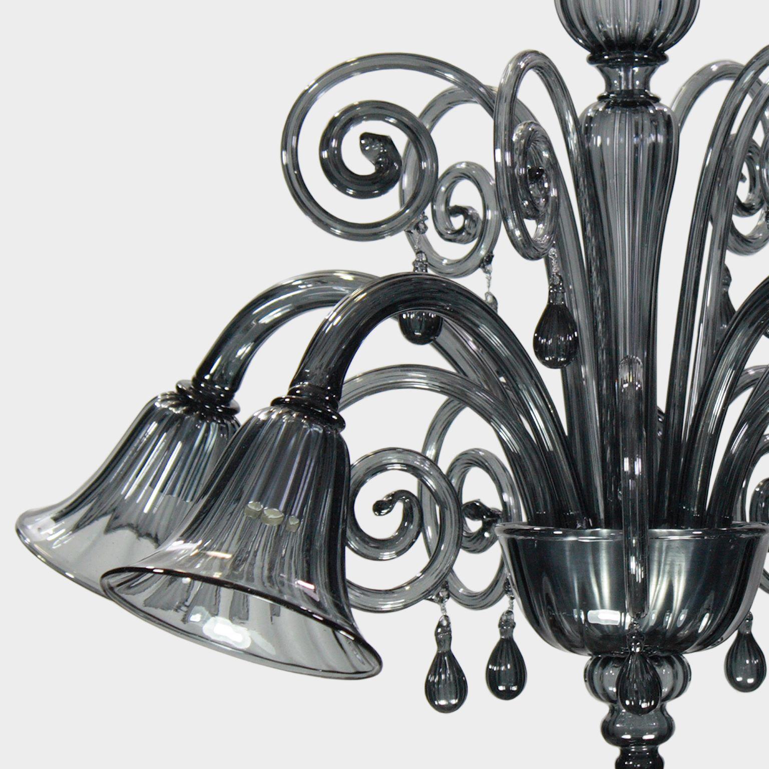 This venetian glass chandelier is in dark grey murano glass has glass pastorals and pendants. The lights are downwards and the main glass parts are realised with the rigadin style.
It is characterized by a romantic and delicate shape. The stem is