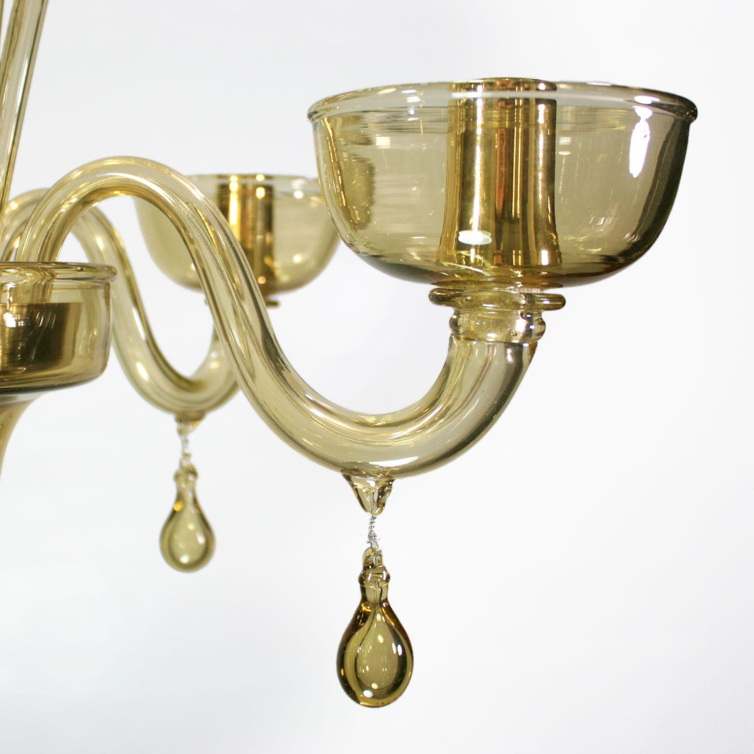 This venetian glass chandelier is in straw smooth Murano glass and has pastorals and pendants. The arms have upwards glass cups.
It is characterized by a romantic and delicate shape. The stem is characterized by shaped glass details. The glass drops