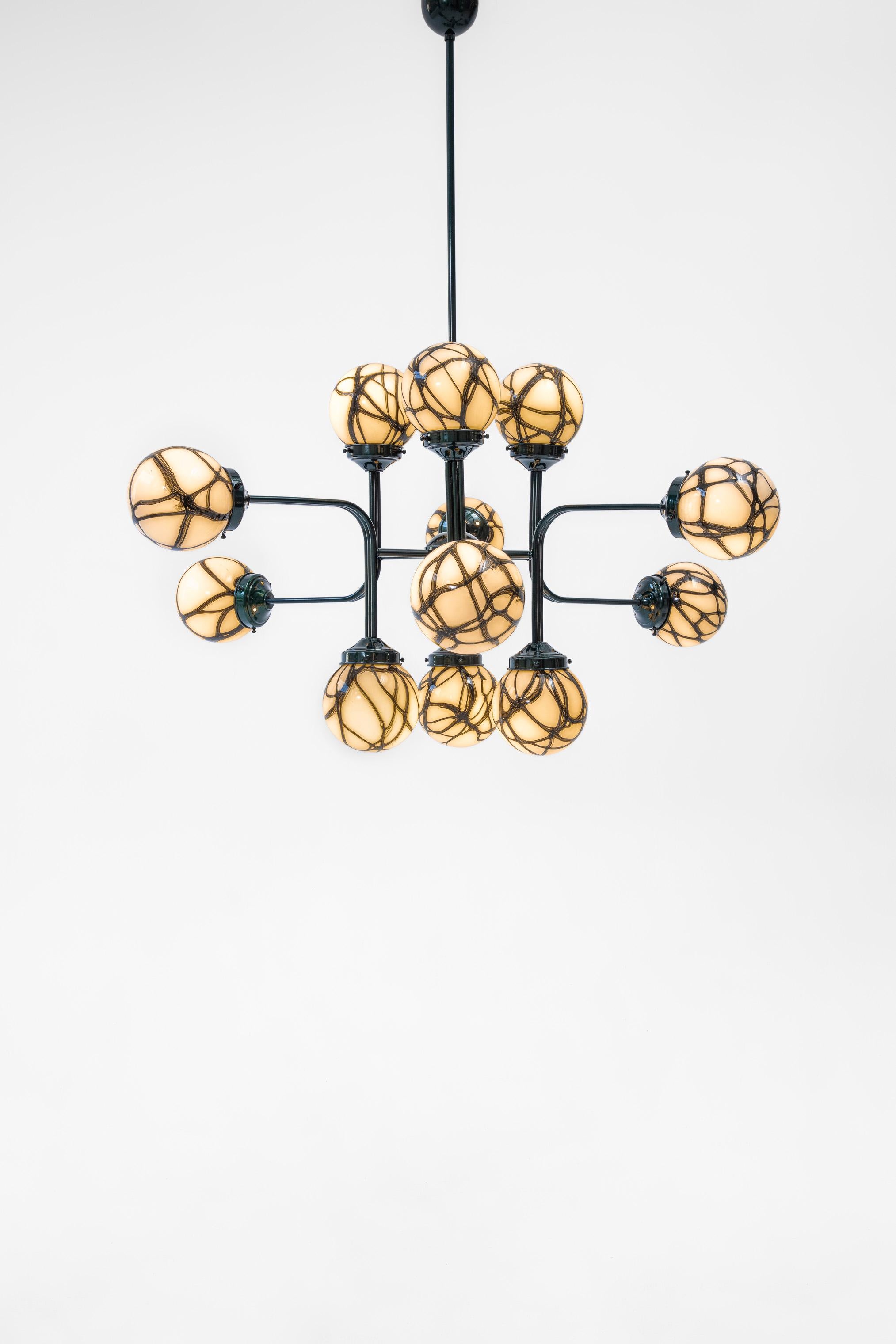 “Ziron” is an entirely handmade chandelier inspired by antique handblown glasses. Each handblown glass dome is unique with different patterns and harmonize with each other in an elegant way. Metallic green painted pieces are bent and connected