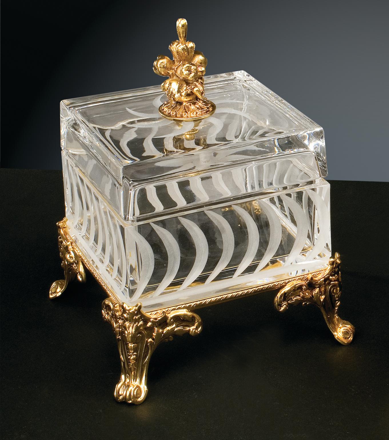 Boîte en cristal clair avec des gravures en taille opaque agrémentées de détails en laiton réalisés selon la technique artisanale de la cire perdue avec une finition en or patiné. Chaque objet est fabriqué à la main et le soin apporté à chaque