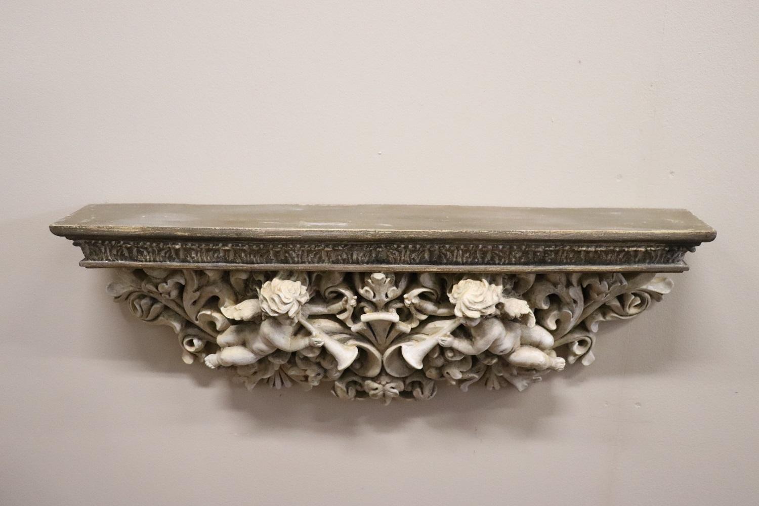 Refined Italian sculpture in composite material recently manufactured. A beautiful wall shelf characterized by an elaborate Baroque style decoration with curls and volutes, in the center two angels playing. The shelf was painted with a particular