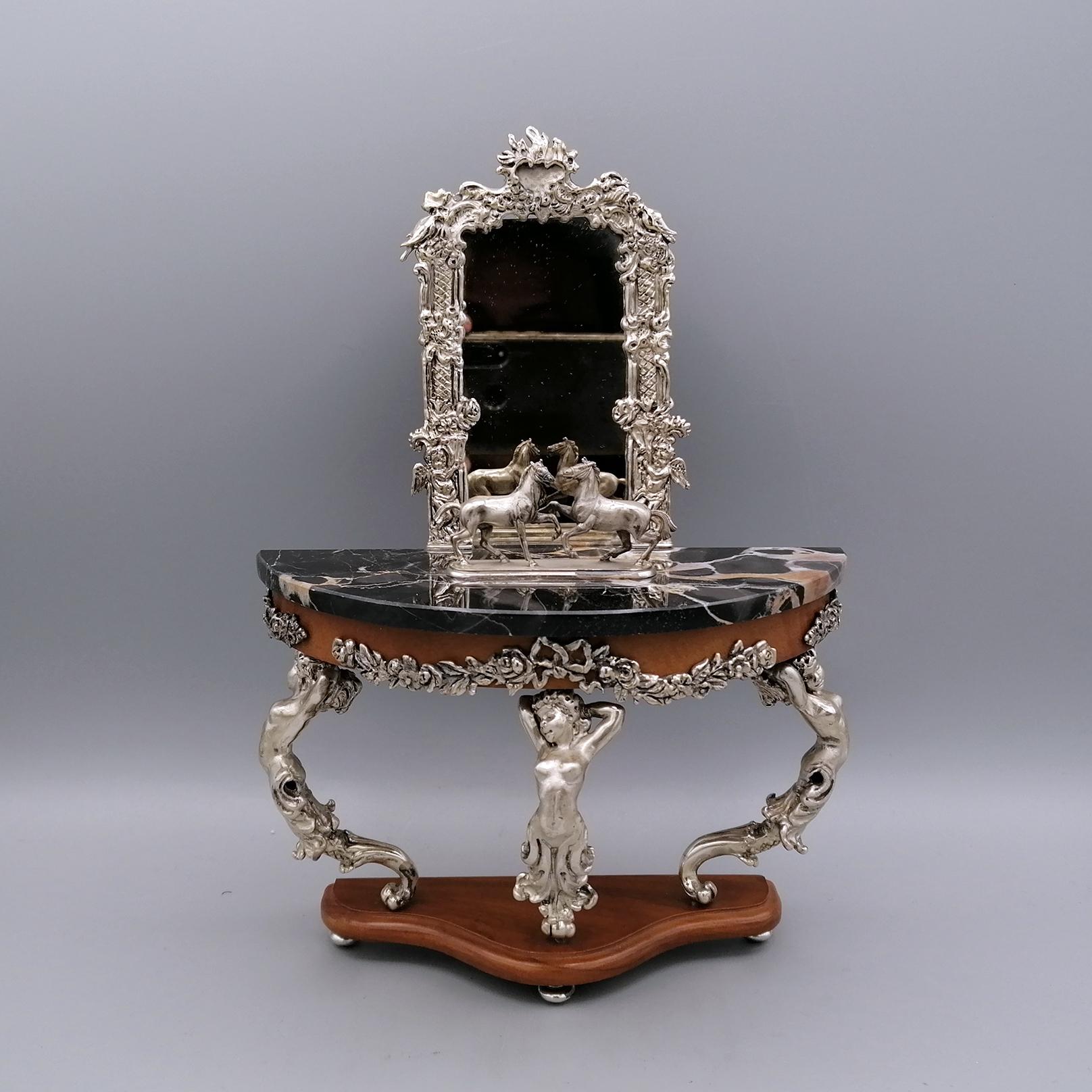 Console miniature in 925 silver with mirror and marble top, wooden details.
This miniature was made in 925 silver with the fusion technique.
The supports under the top depict three sirens while the friezes on the wood are festoons with flowers and