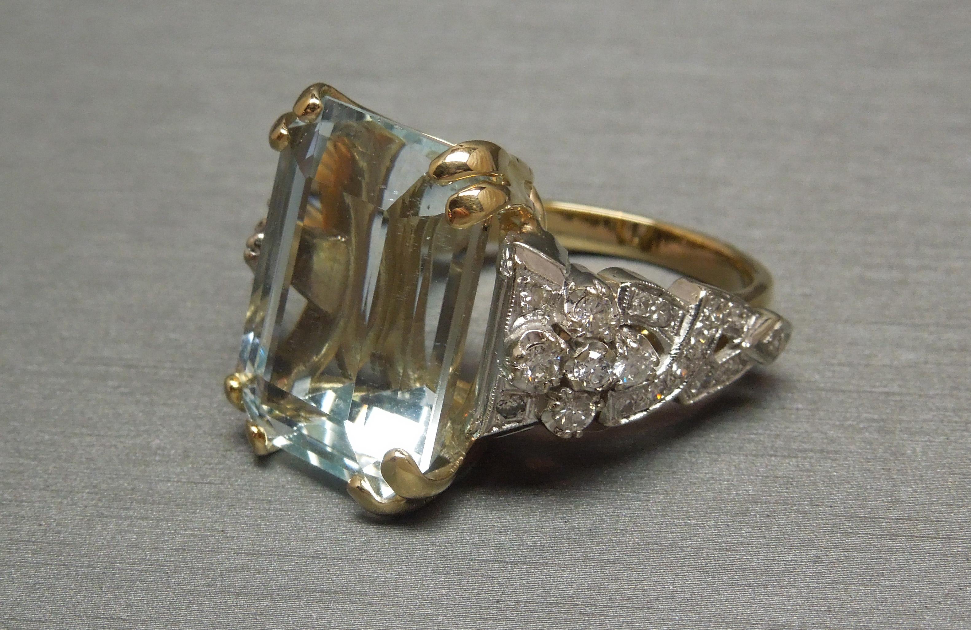 A central 22.50 carat GIA Certified Aquamarine in an opulent Emerald cut secured in 4 Doubled 14KT Yellow Gold prongs with Diamonds set at each side section in 14KT White Gold Art Deco designs consisting of Nearly Colorless Nearly Flawless Single